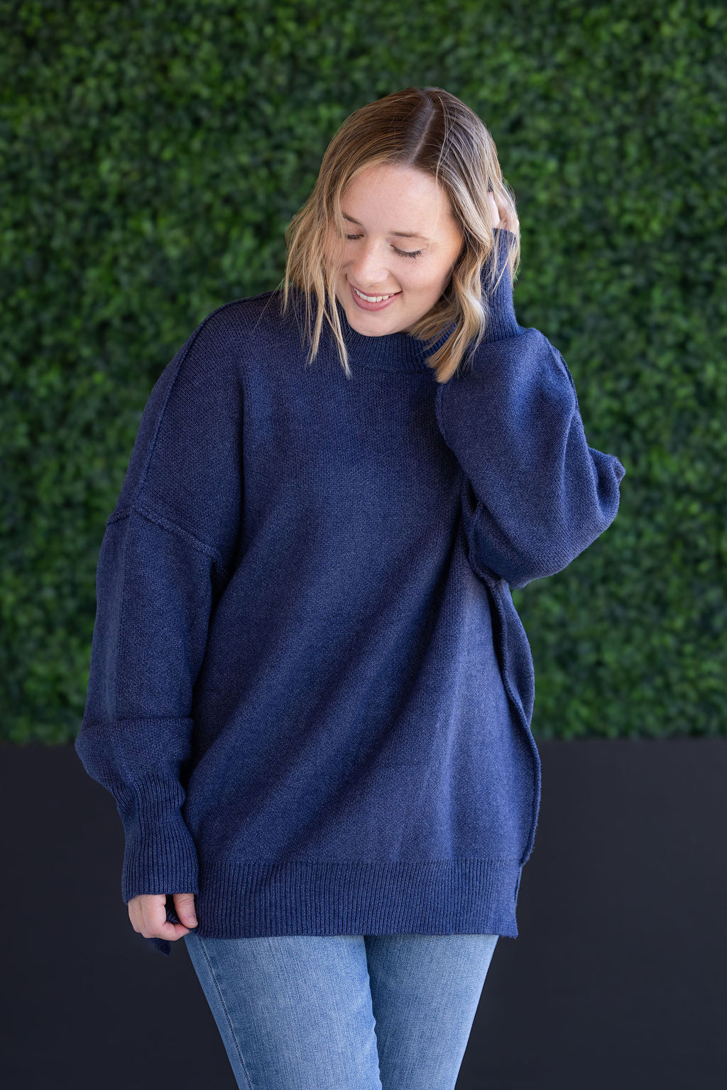 Woman wearing oversized navy mock neck sweater with thick seam detailing, ribbed cuffs, and relaxed fit