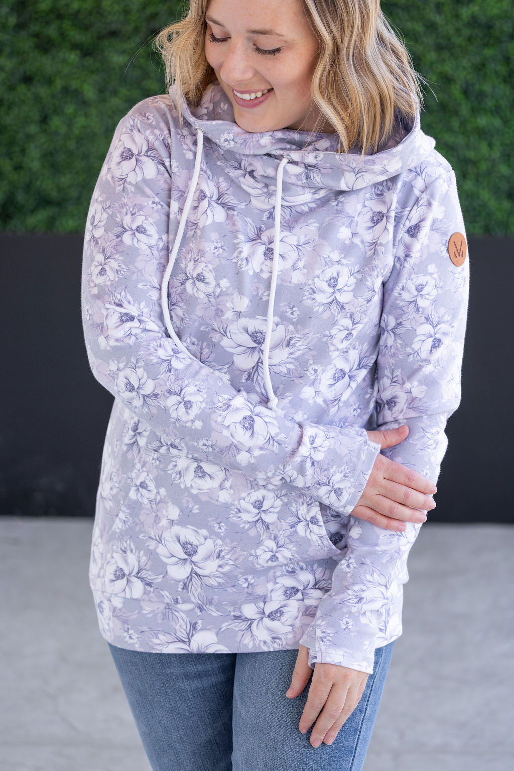 Woman wearing gray floral hoodie with cowl neck, drawstrings, thumbholes, and kangaroo pocket