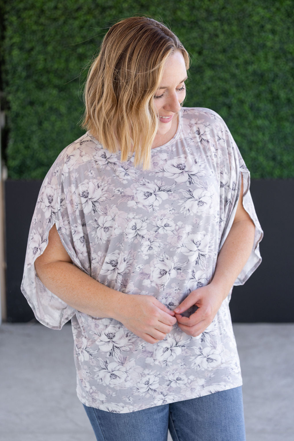 Woman wearing gray dolman sleeve top with white floral print, flowy sleeves, and relaxed silhouette