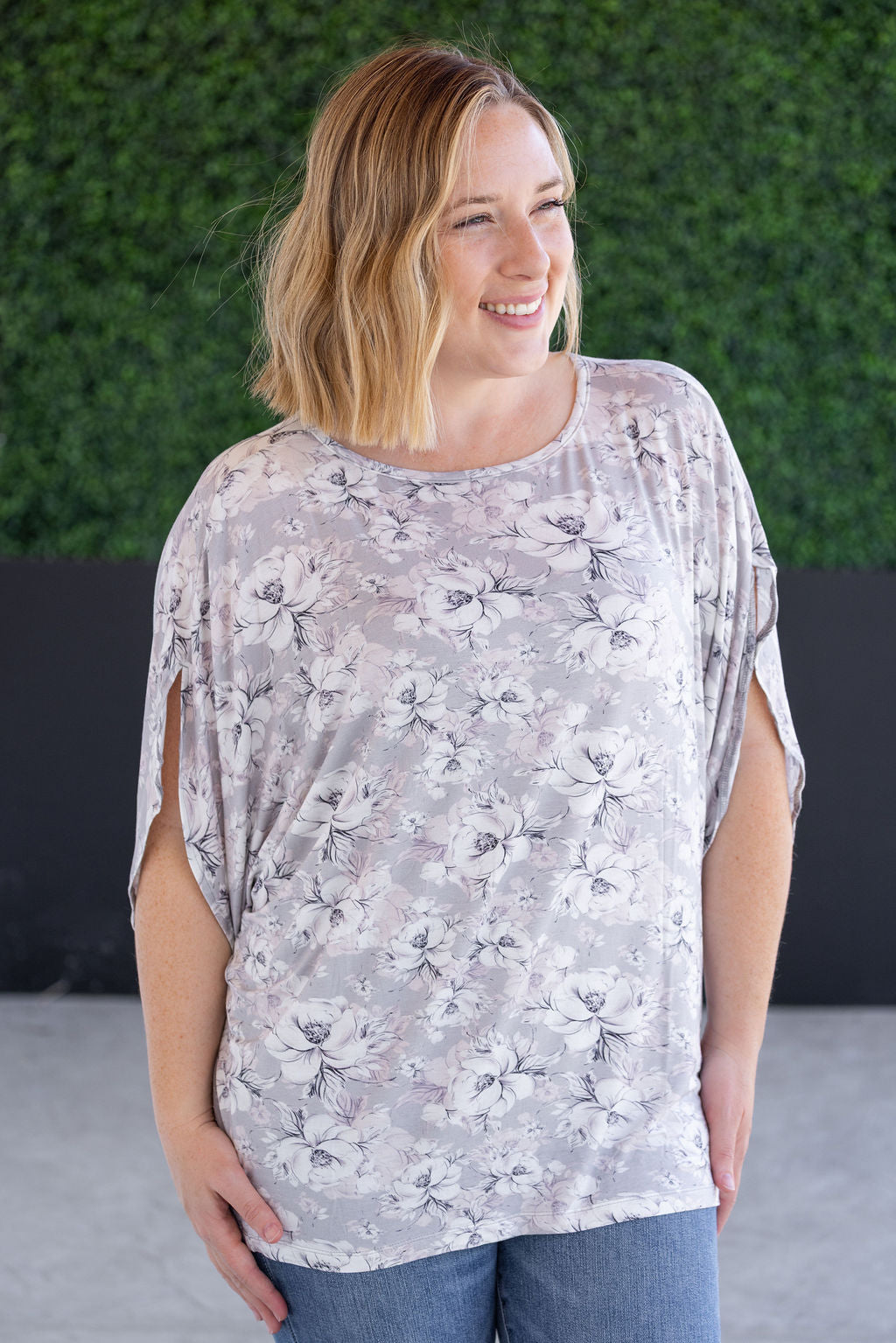 Woman wearing gray dolman sleeve top with white floral print, flowy sleeves, and relaxed silhouette