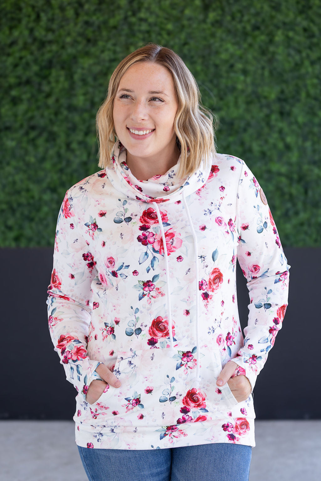 Woman wearing white funnel neck sweatshirt with pink floral print, drawstring neckline, and kangaroo pocket
