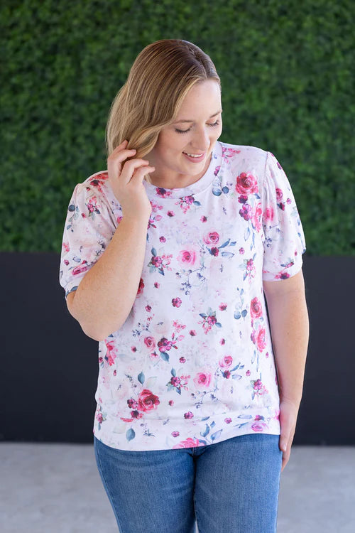 Woman wearing white top with pink floral print, puff sleeves, and rounded crew neckline