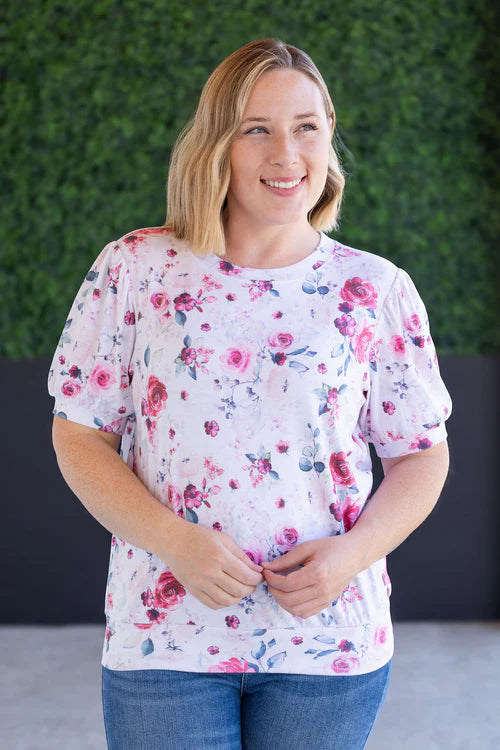 Woman wearing white top with pink floral print, puff sleeves, and rounded crew neckline