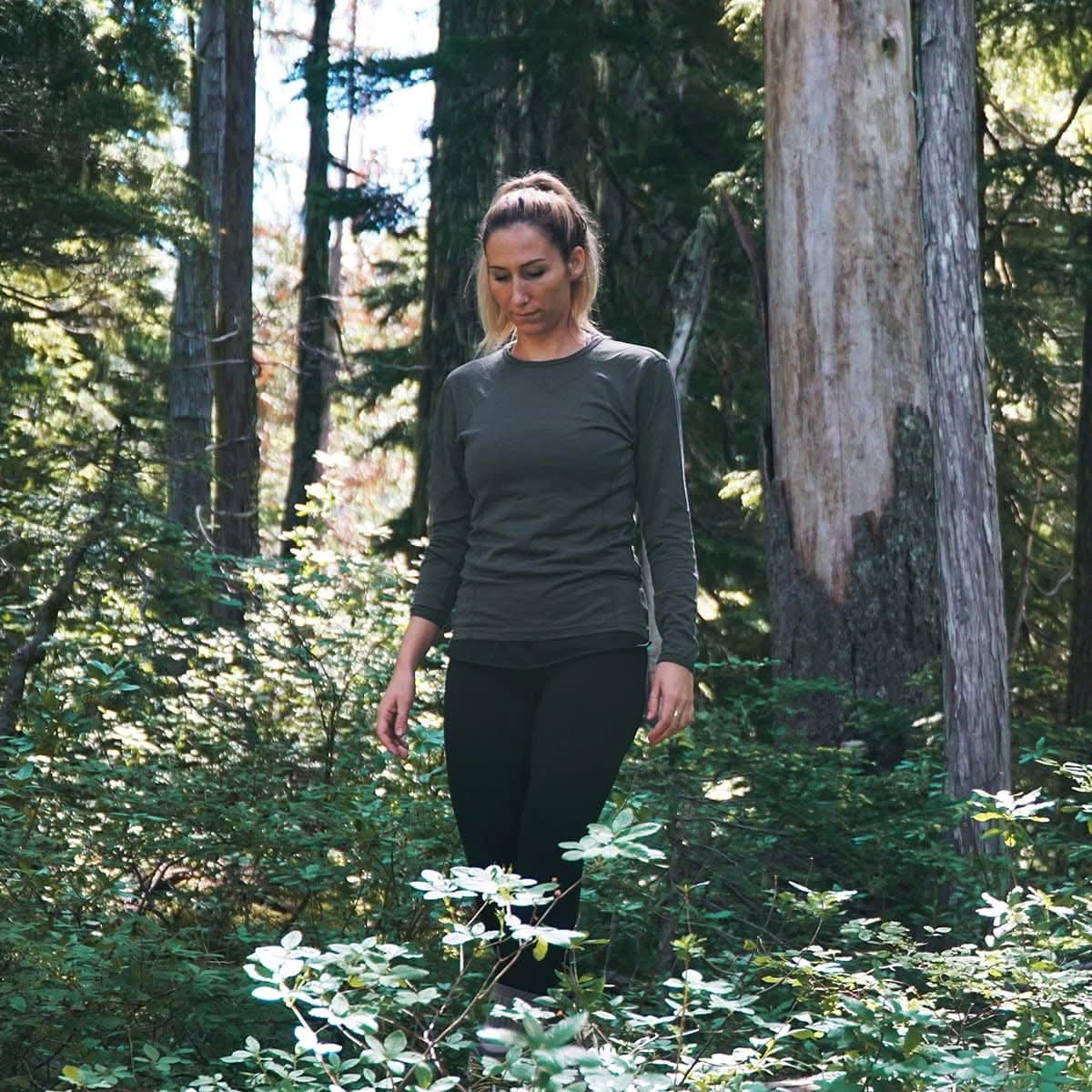 Woman walking through a forest wearing a charcoal long-sleeve shirt and black pants.