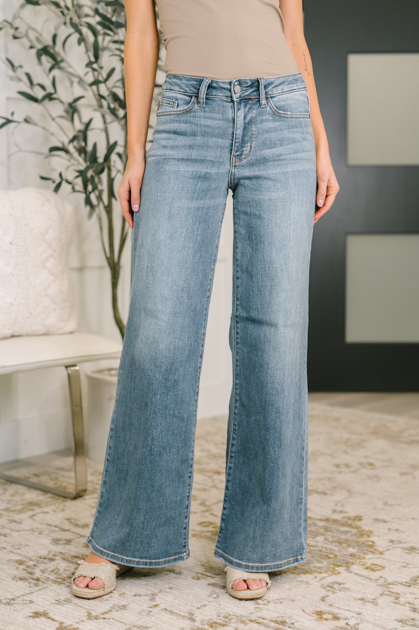 Woman wearing light wash mid rise wide leg jeans with retro silhouette and taupe top
