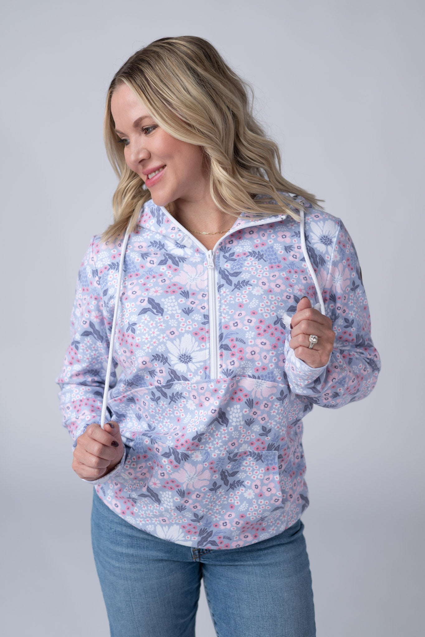 Woman wearing a Half Zip Hoodie in Ditsy Blush Floral with periwinkle blue background and pink and white flowers, featuring a kangaroo pocket and hood with drawstrings