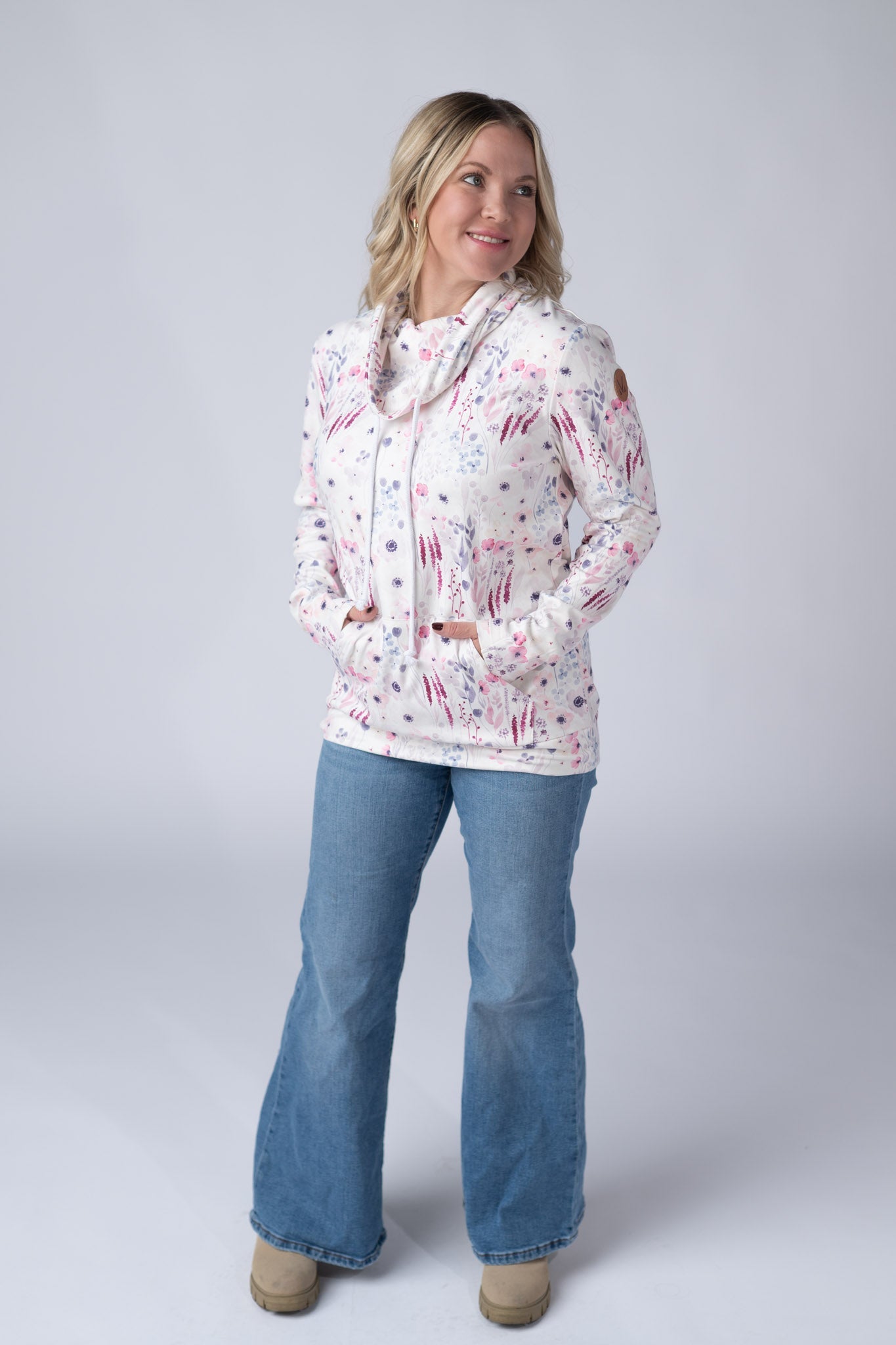 Woman wearing a white Soft Funnel Neck Sweatshirt with watercolor Wildflower Gardens print in pink, purple, and magenta, featuring a funnel neck with drawstrings and kangaroo pocket