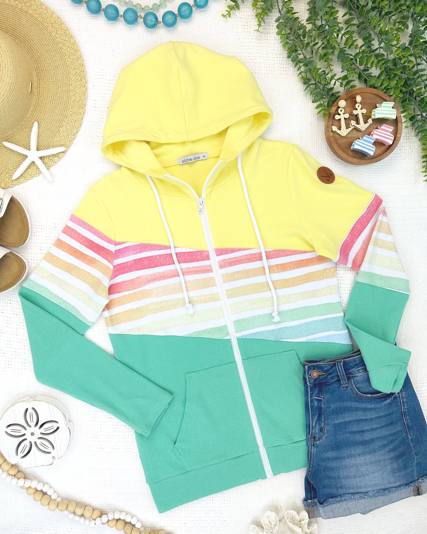 Colorful striped hoodie with a hood, denim shorts, and beach accessories on a light surface.