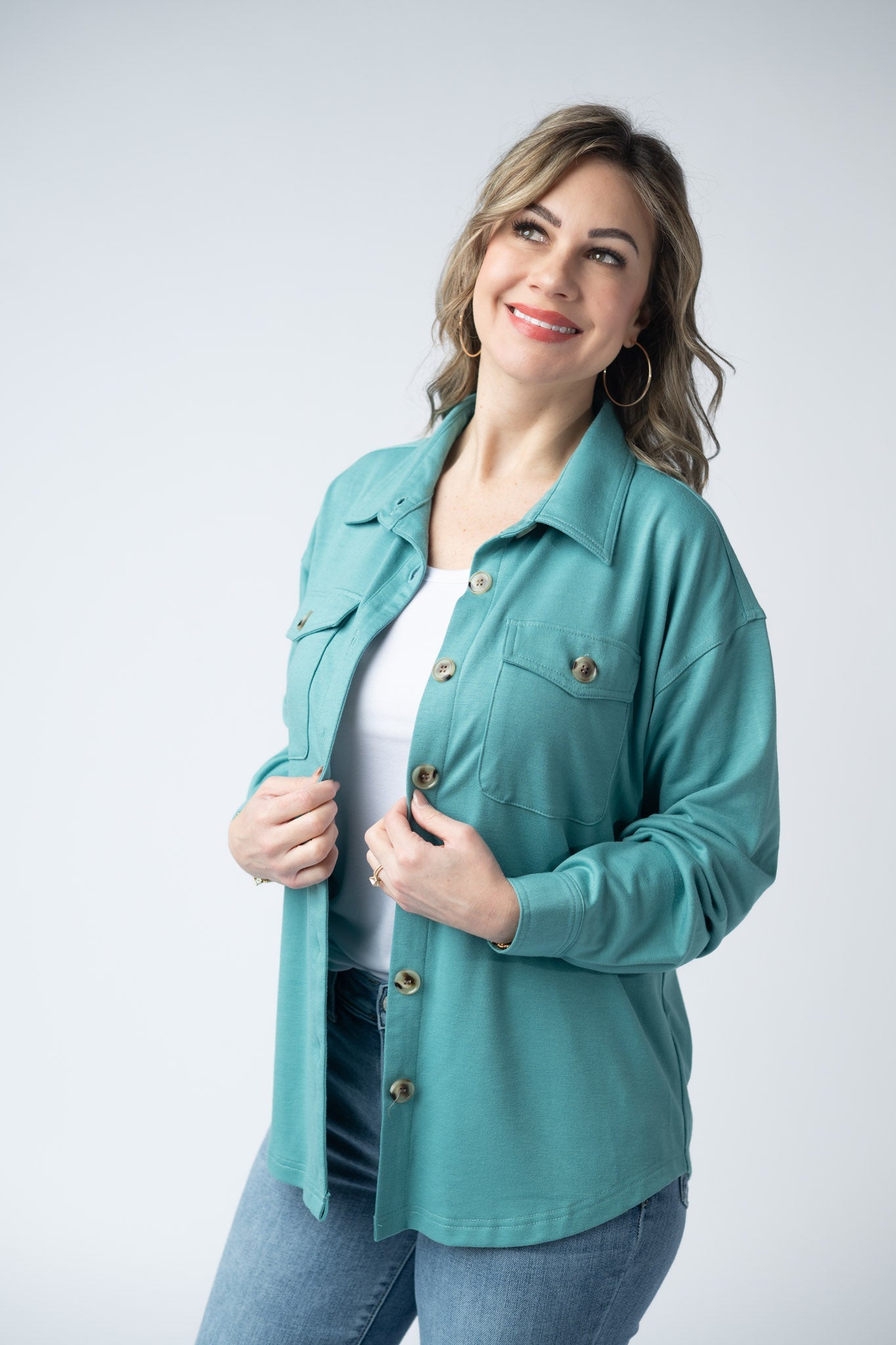 Woman wearing a teal Brenna Button Down Top with breast pockets and button front, styled open over a white tank with jeans