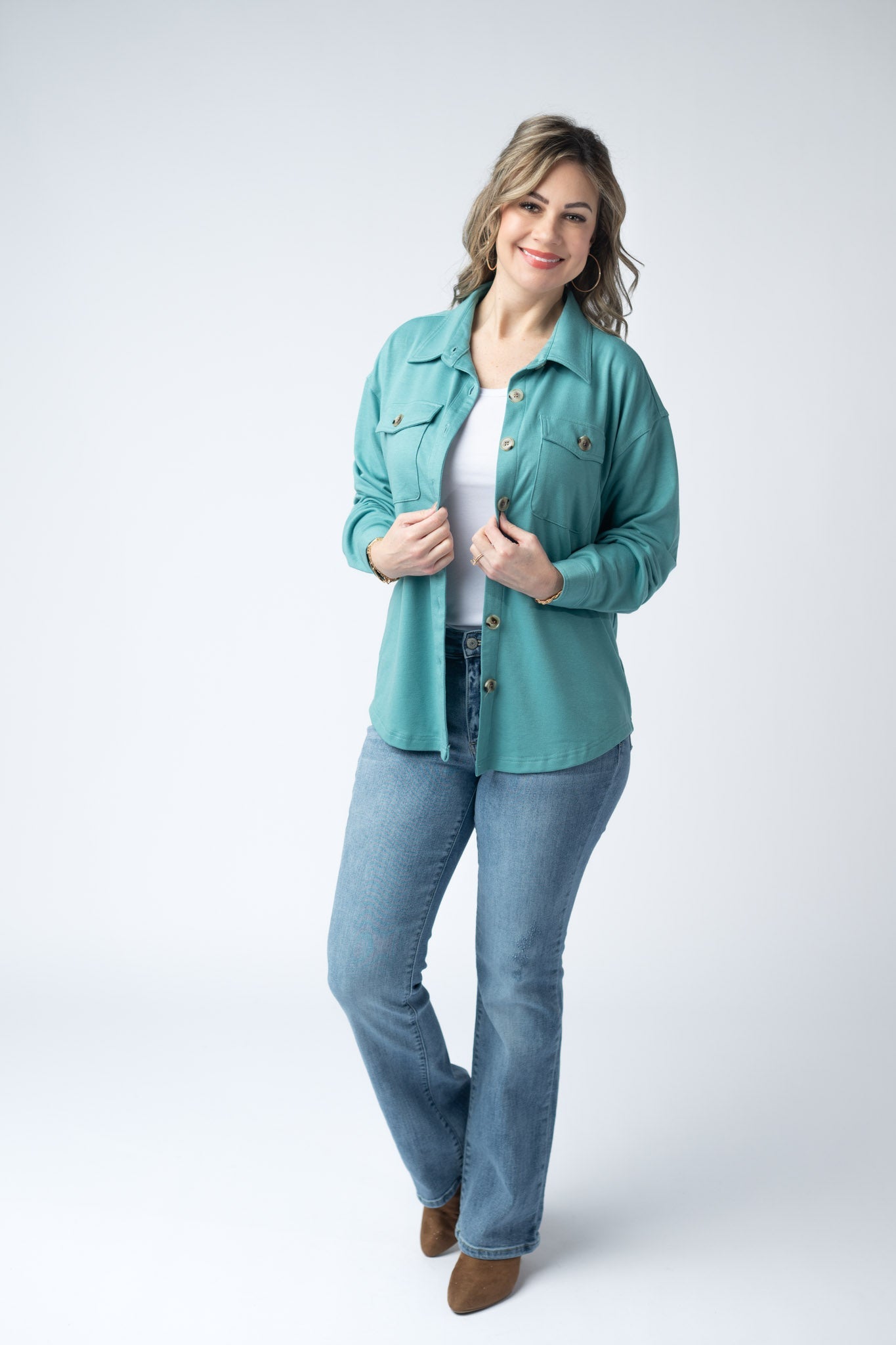 Woman wearing a teal Brenna Button Down Top with breast pockets and button front, styled open over a white tank with jeans
