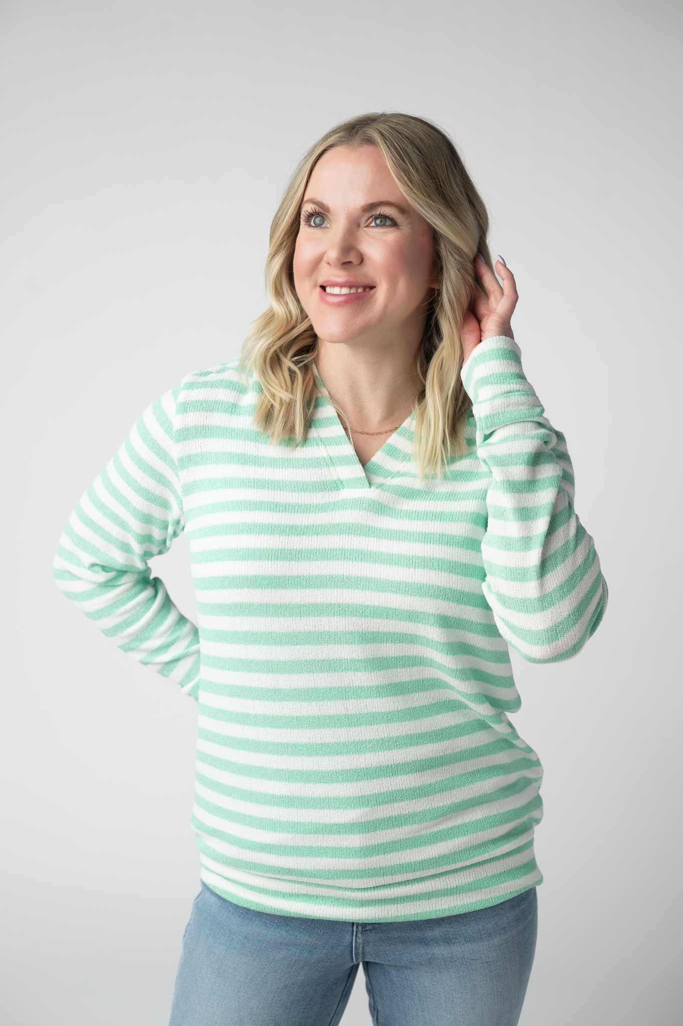 Woman wearing the Michelle Mae Amelia Striped Hoodie in Green, a lightweight green and white striped open-knit hoodie with cuffed sleeves and a V-neckline