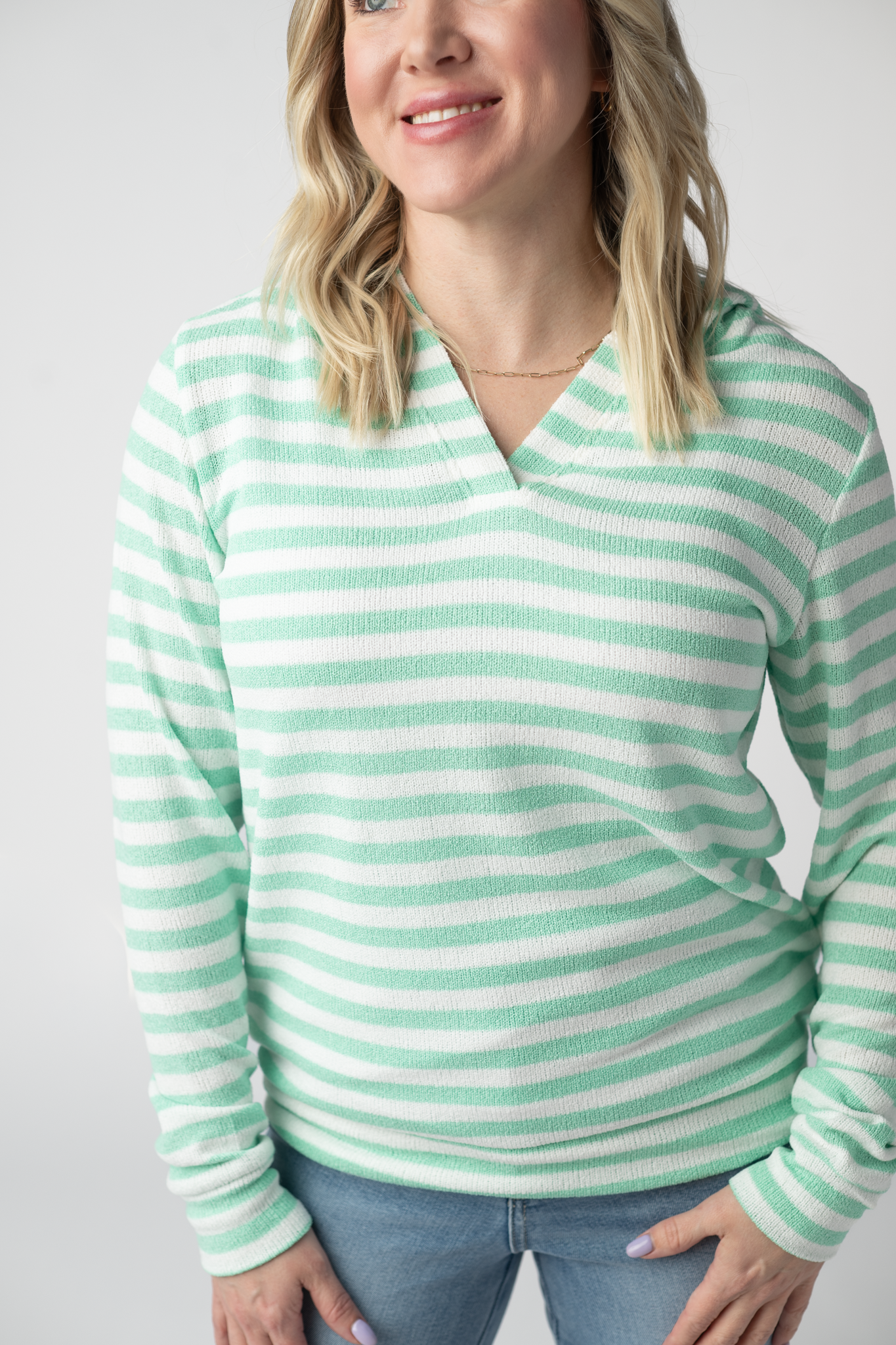 Woman wearing the Michelle Mae Amelia Striped Hoodie in Green, a lightweight green and white striped open-knit hoodie with cuffed sleeves and a V-neckline