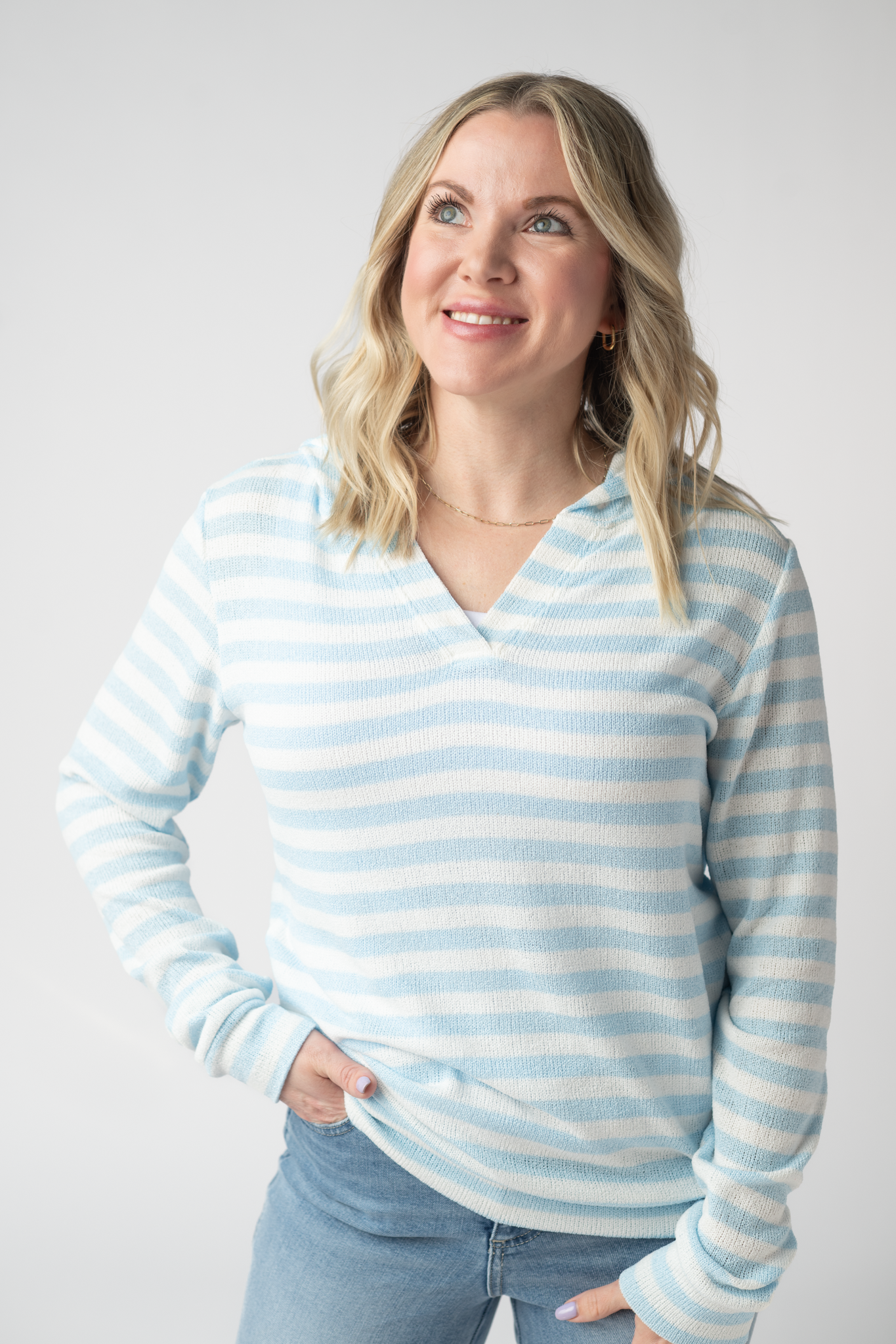 Woman wearing the Michelle Mae Amelia Striped Hoodie in Sky Blue, a lightweight blue and white striped open-knit hoodie with cuffed sleeves and a V-neckline