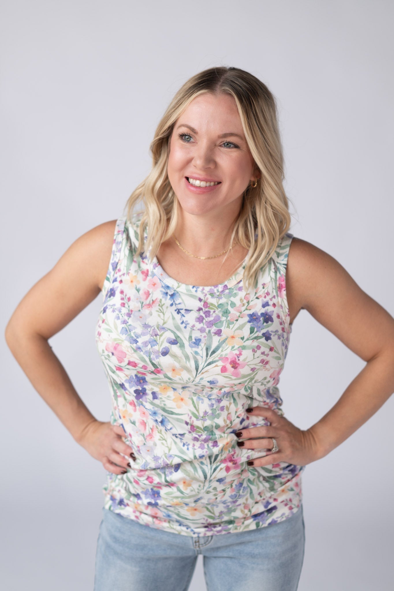 Woman wearing a white Ava Tank with bright watercolor cottage floral print in blue, purple, pink, yellow, and green, paired with jeans