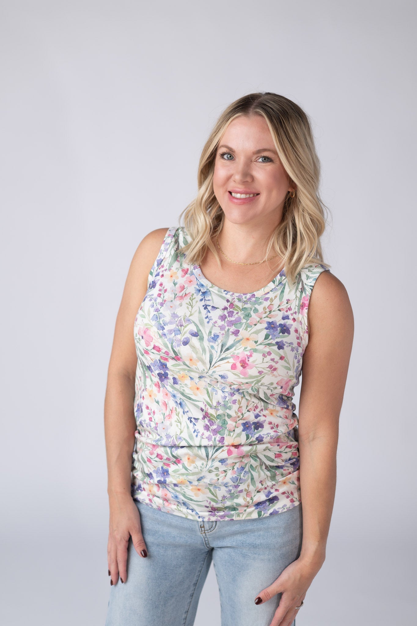 Woman wearing a white Ava Tank with bright watercolor cottage floral print in blue, purple, pink, yellow, and green, paired with jeans