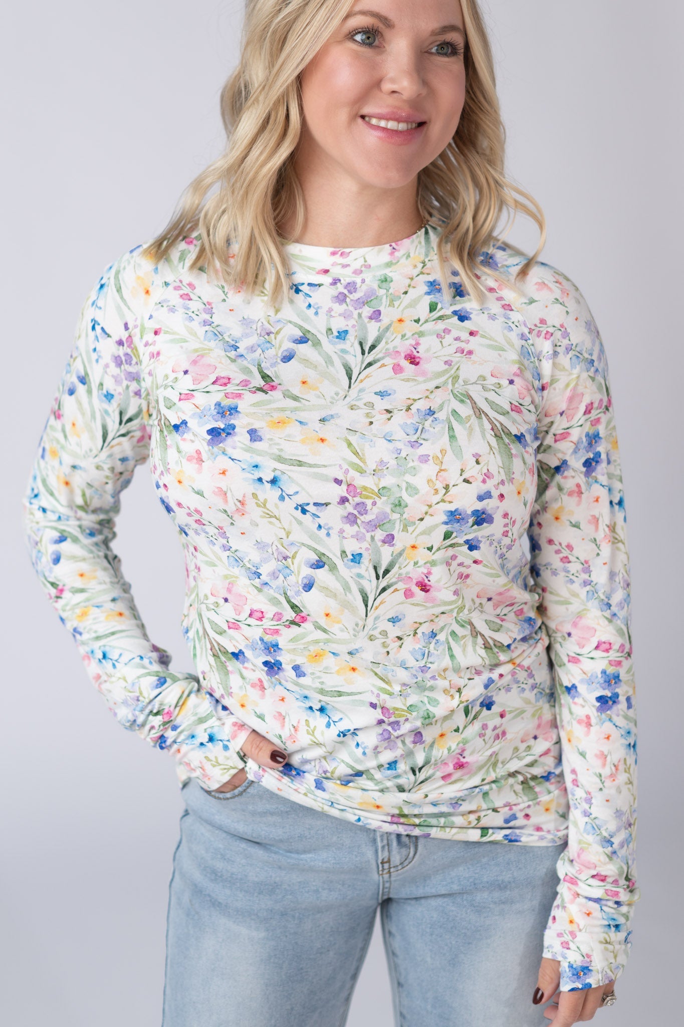 Woman wearing a white Blair Long Sleeve Top with bright watercolor cottage floral print in blue, purple, pink, yellow, and green, paired with jeans
