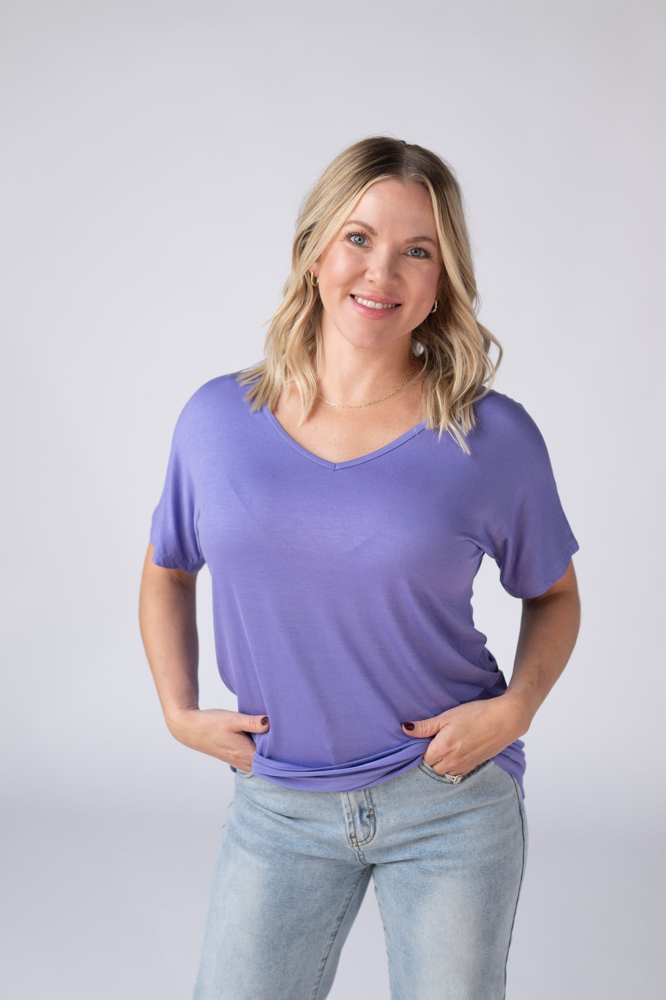 Woman wearing a periwinkle purple Chloe Cozy Tee with v-neckline and dolman sleeves, paired with jeans