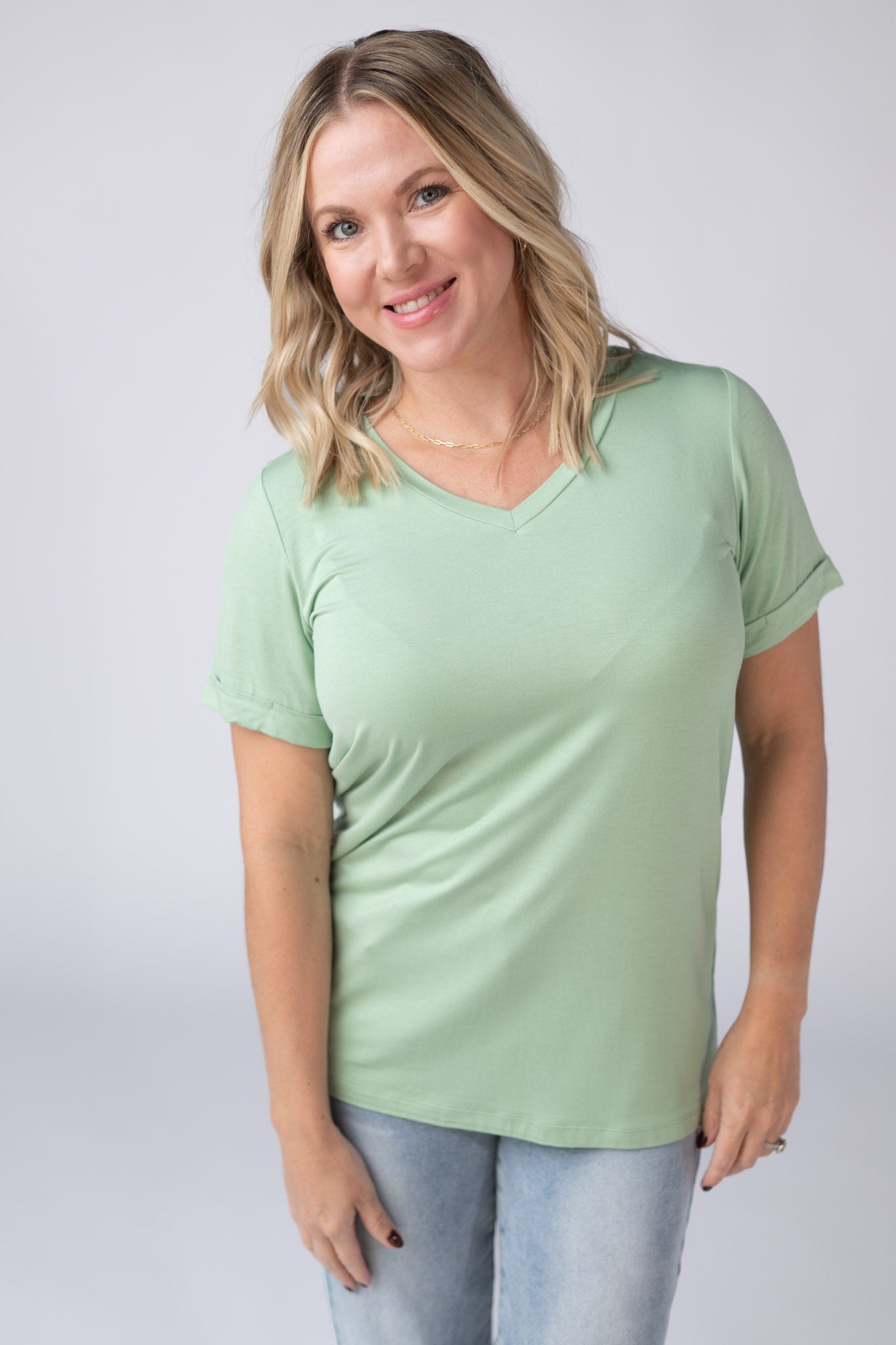 Woman wearing a seafoam green Sophie Tee with v-neckline and cuffed sleeves, paired with jeans