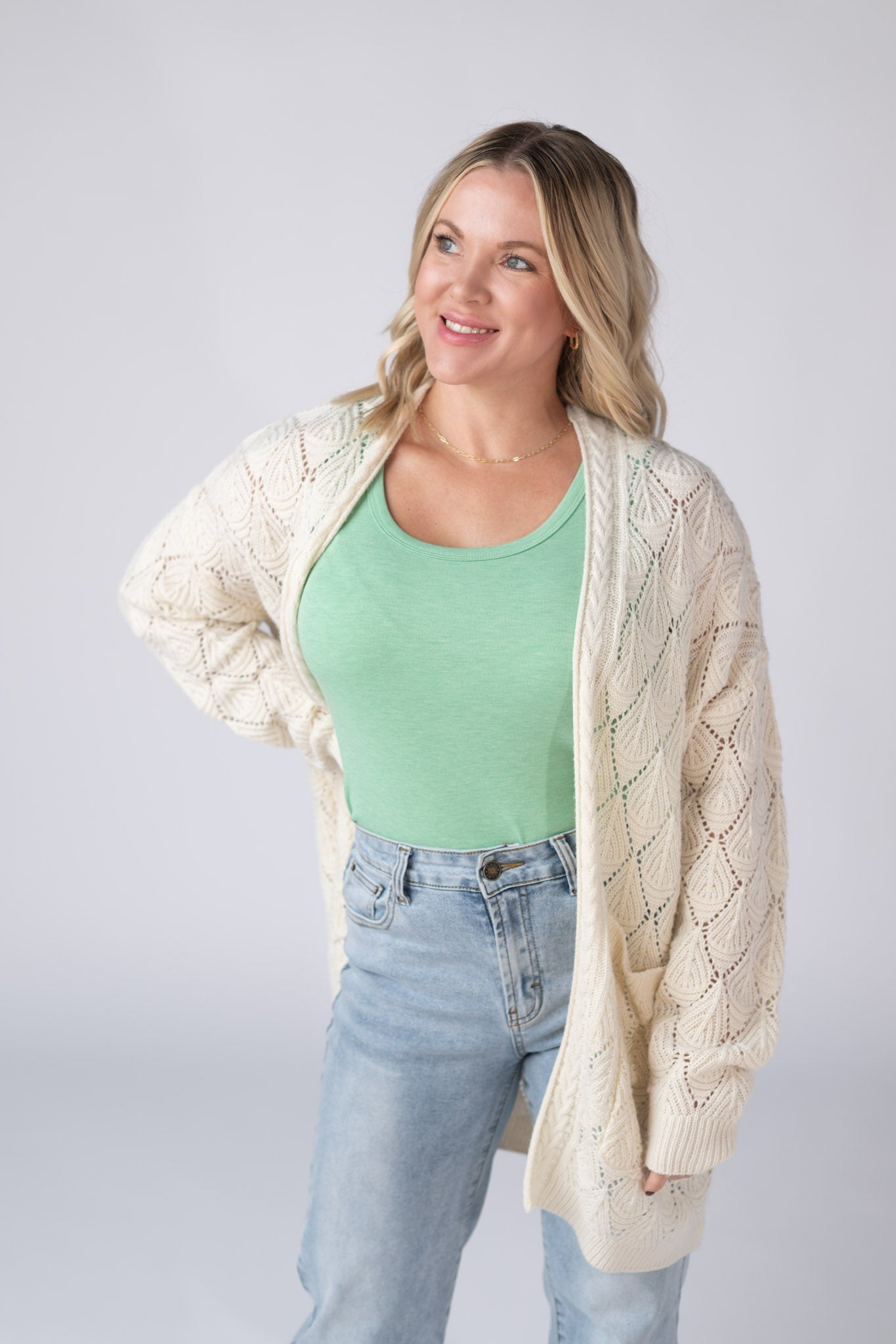 Woman wearing an ivory Open Knit Cardigan with leaf pattern detail and pockets, layered over a tank and jeans