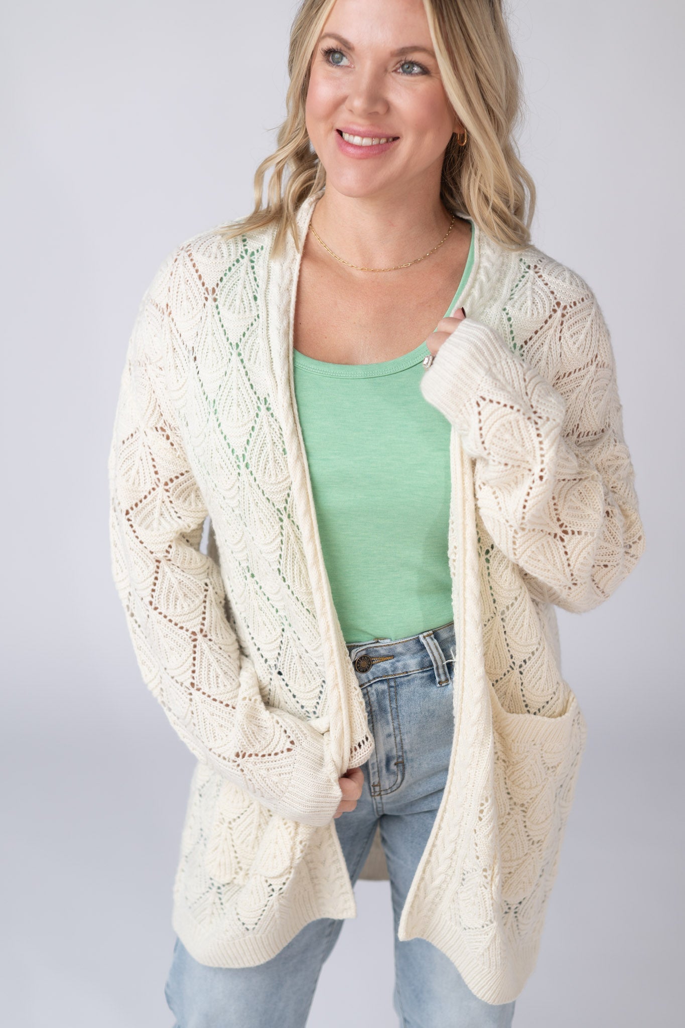 Woman wearing an ivory Open Knit Cardigan with leaf pattern detail and pockets, layered over a tank and jeans