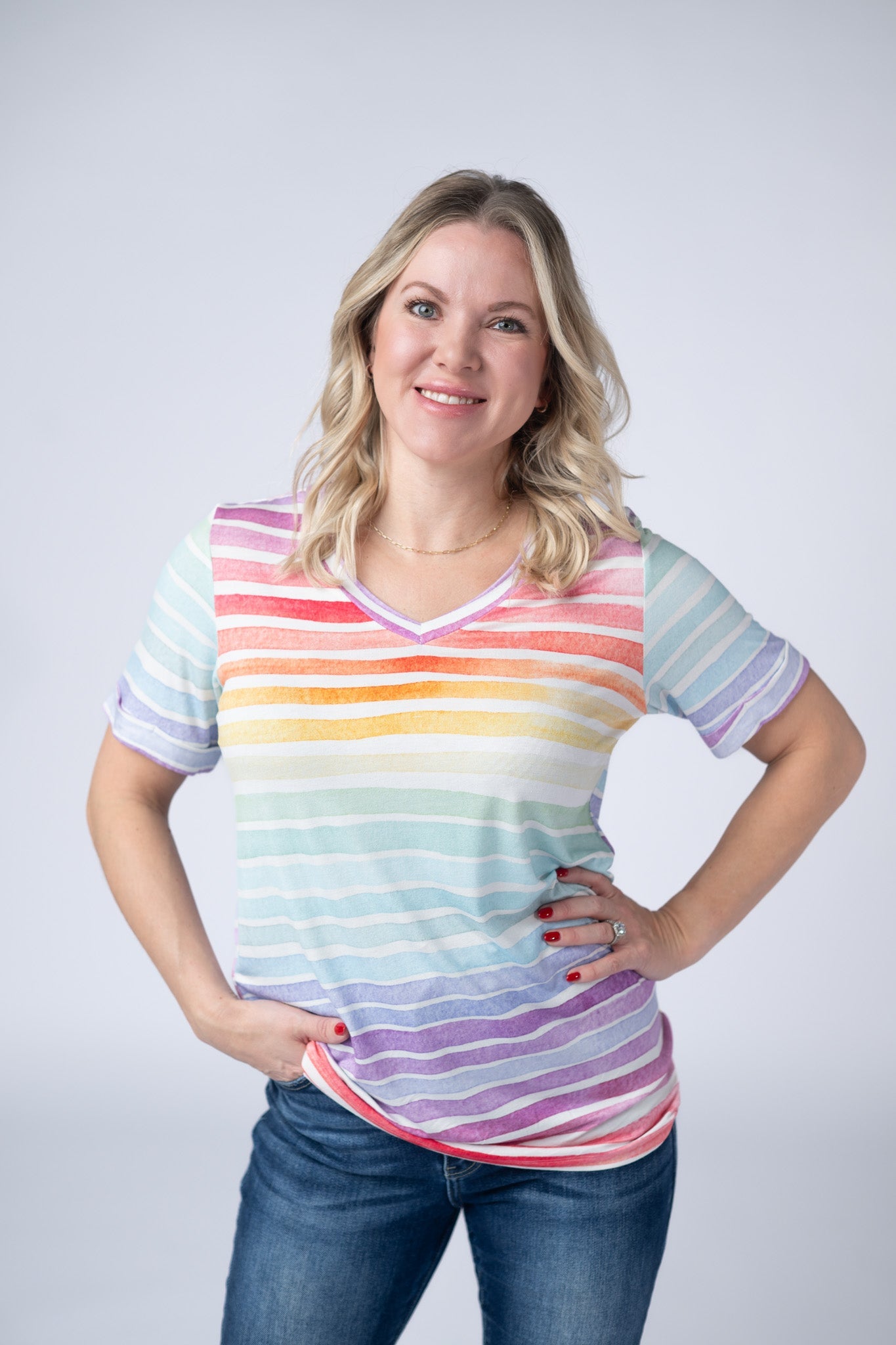 Woman wearing the Michelle Mae Sophie Tee in Rainbow Stripes, a colorful watercolor-style rainbow striped v-neck tee with cuffed sleeves