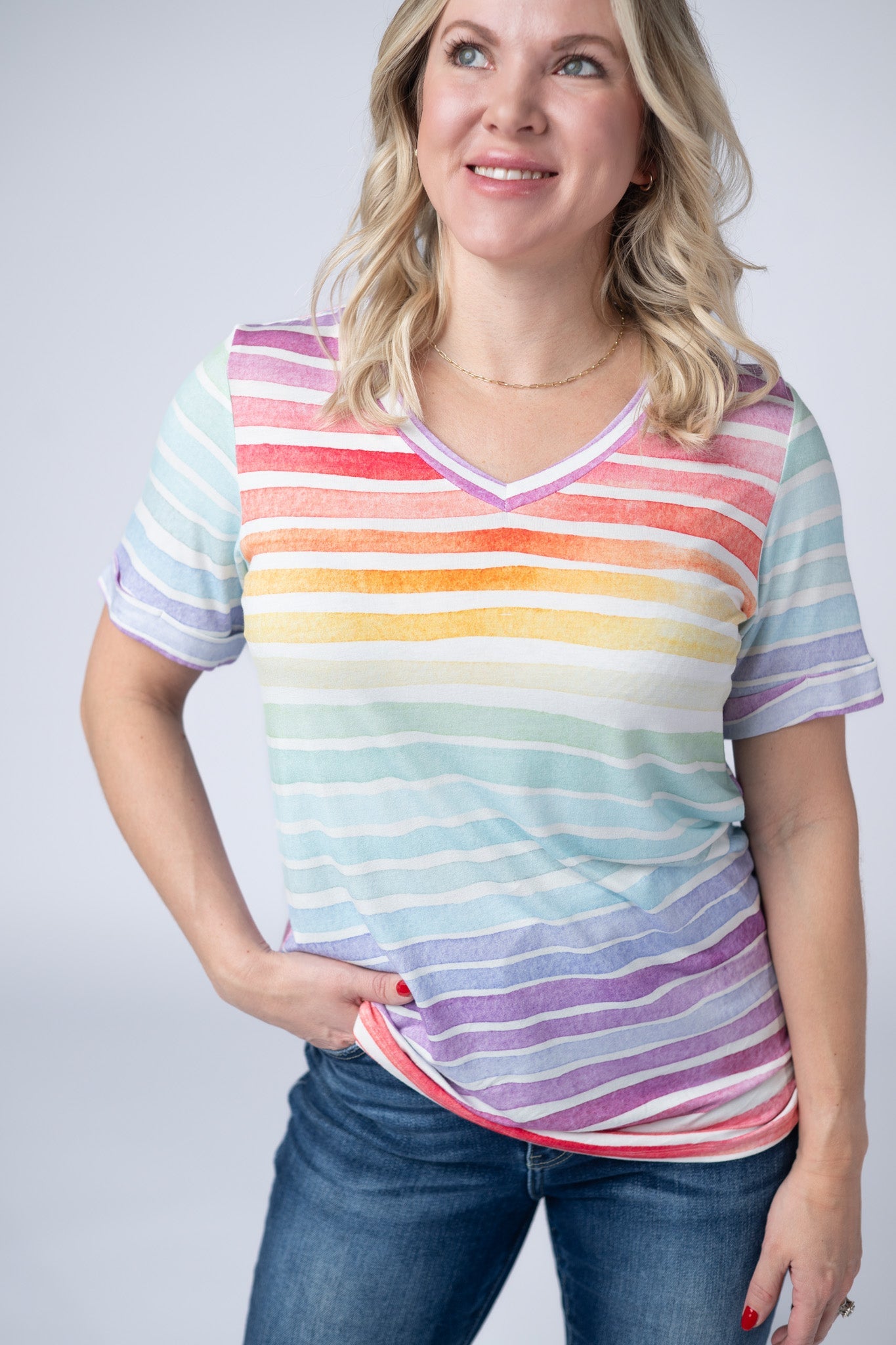 Woman wearing the Michelle Mae Sophie Tee in Rainbow Stripes, a colorful watercolor-style rainbow striped v-neck tee with cuffed sleeves