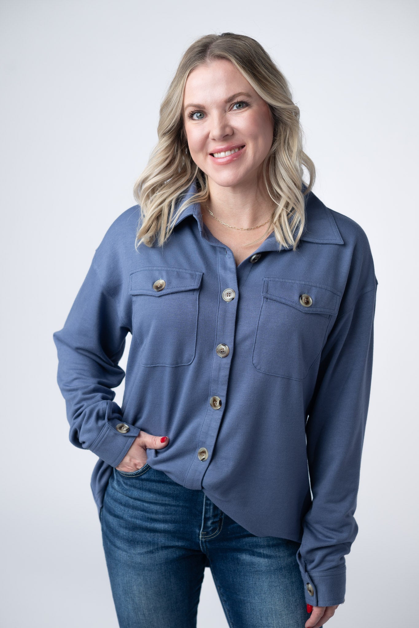 Woman wearing a denim blue Brenna Button Down Top with breast pockets and button front, paired with jeans