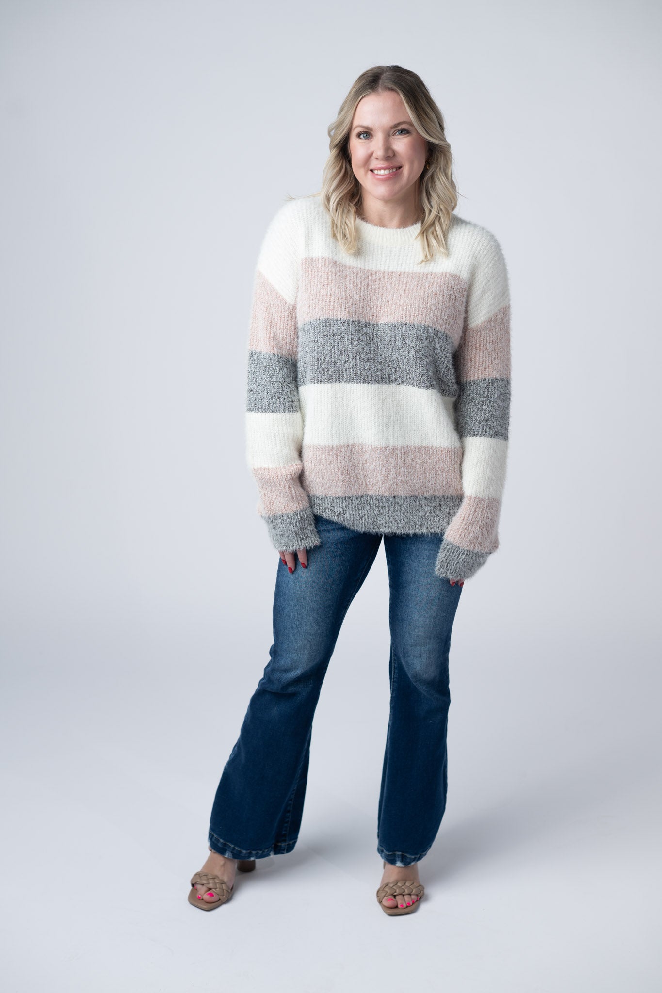 Woman wearing ultra-soft fuzzy colorblock sweater with ivory, blush pink, and gray stripes and crew neckline