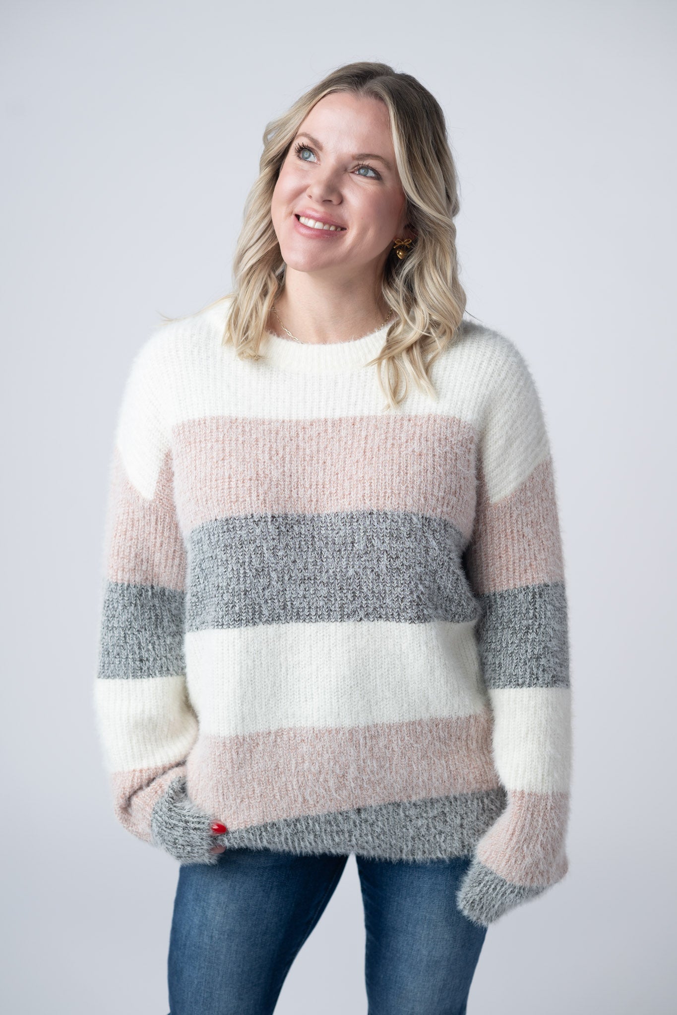 Woman wearing ultra-soft fuzzy colorblock sweater with ivory, blush pink, and gray stripes and crew neckline