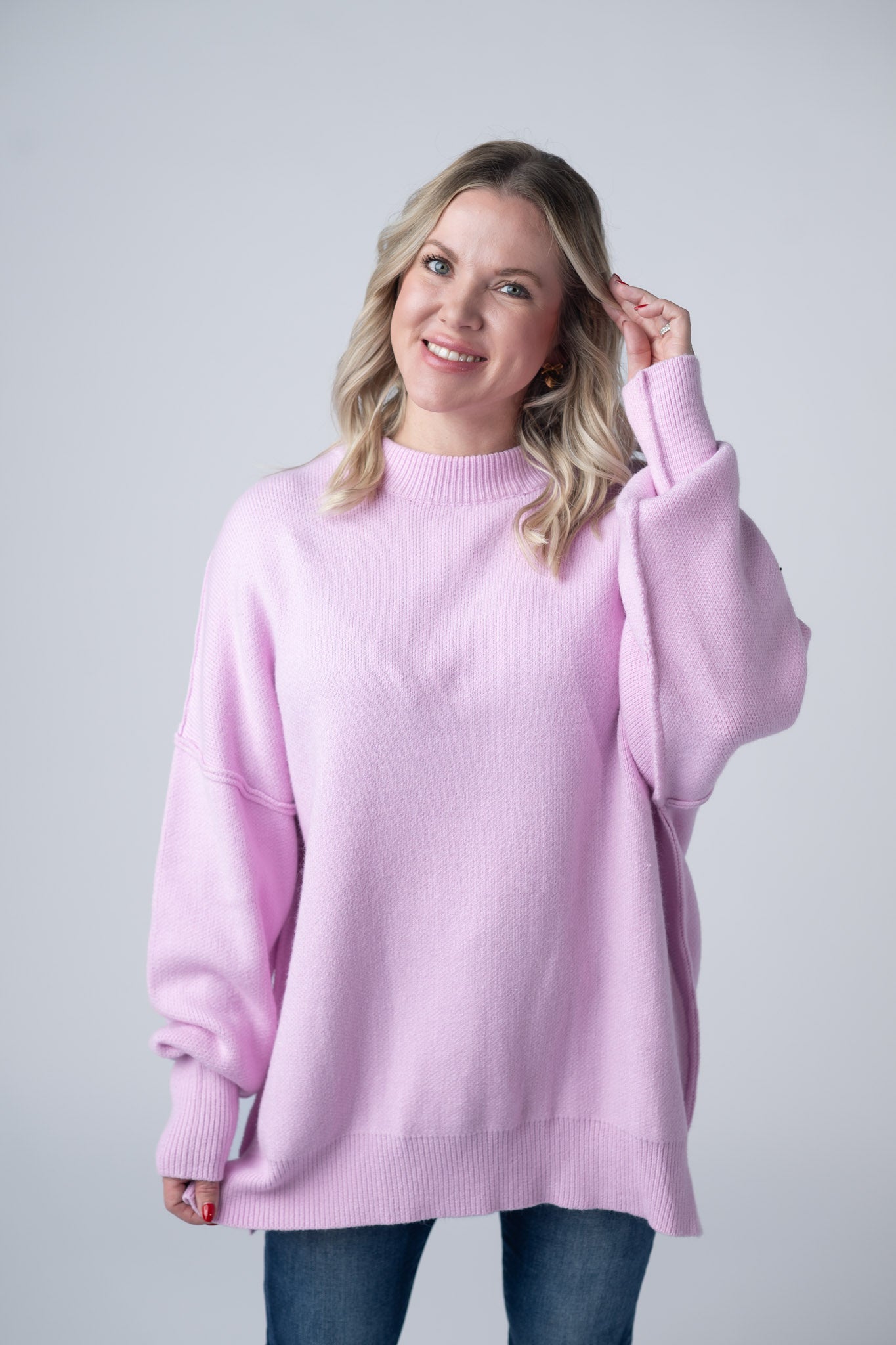 Woman wearing oversized lilac mock neck sweater with thick seam detailing, ribbed cuffs, and relaxed fit