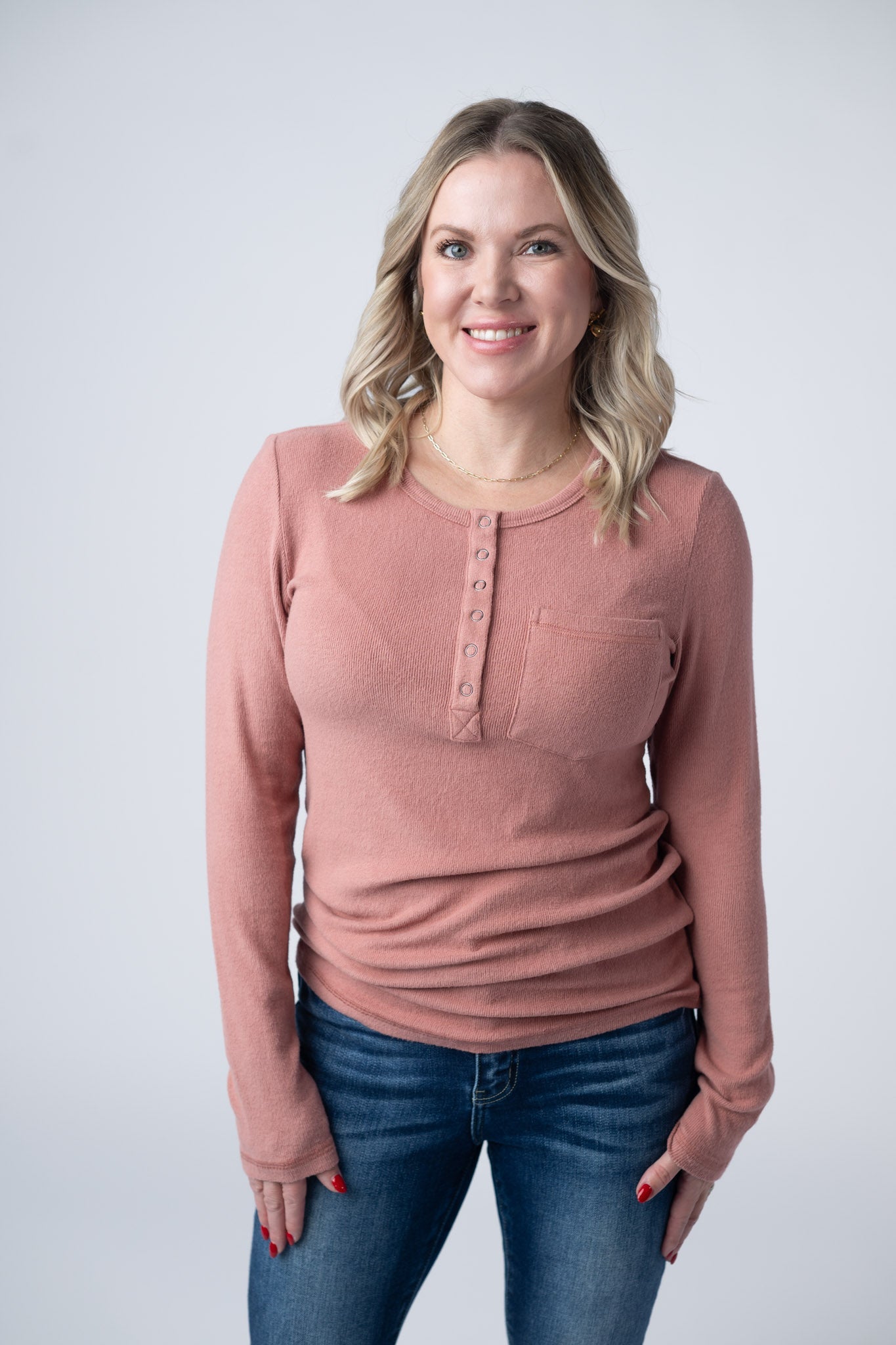 Woman wearing rose pink long sleeve henley top with button snap placket and breast pocket