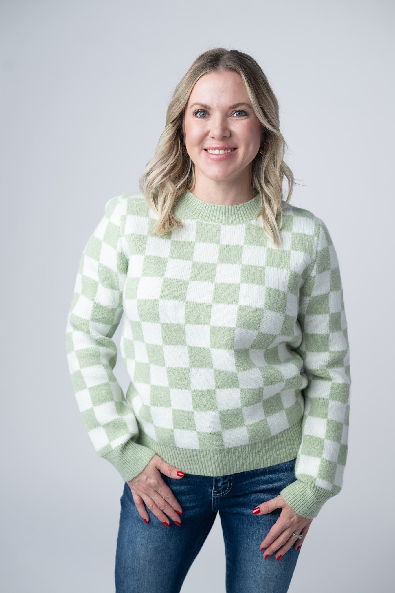 Woman wearing a sage green and white Checkered Sweater with crew neckline and ribbed cuffs, paired with jeans