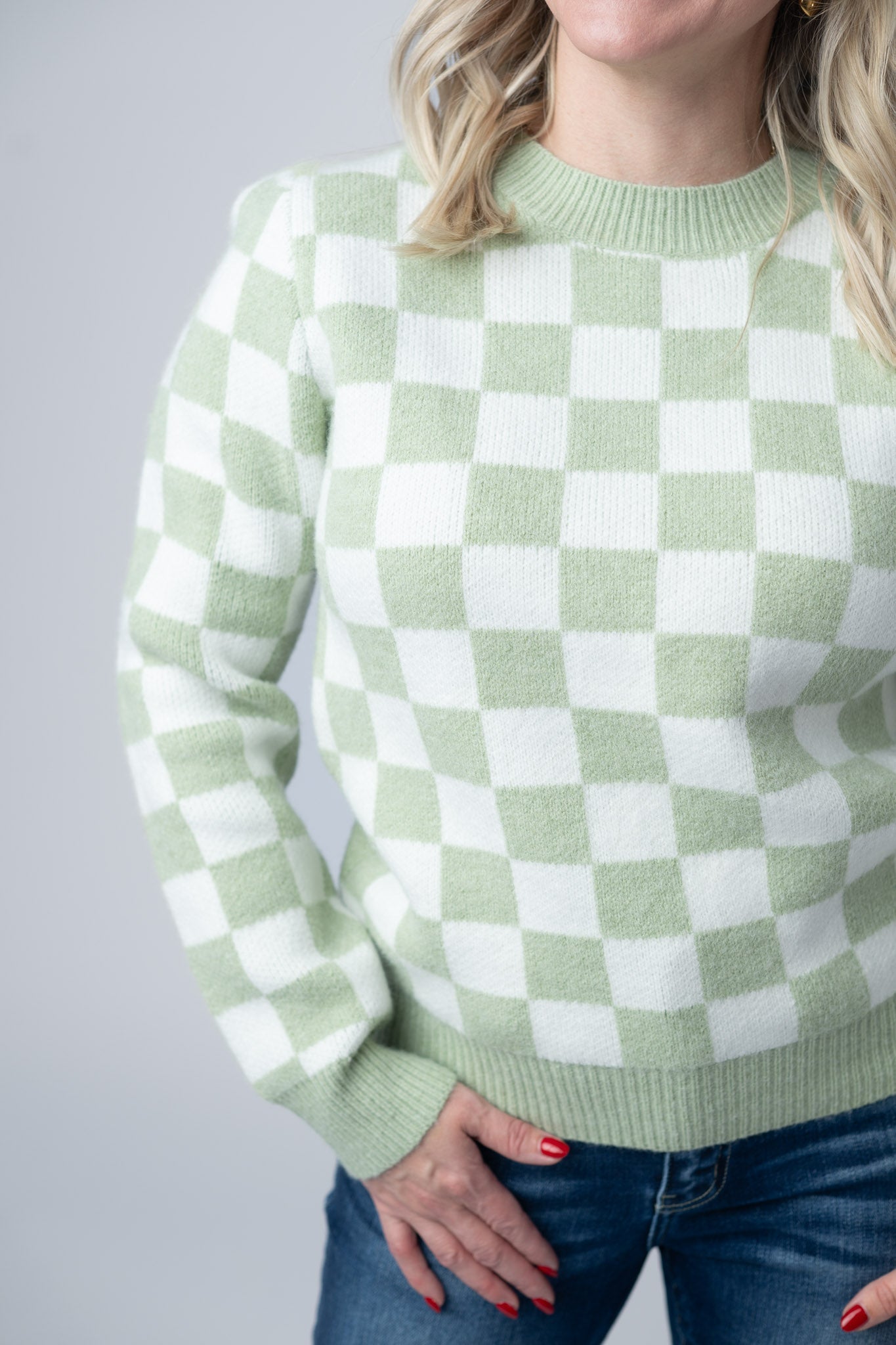 Woman wearing a sage green and white Checkered Sweater with crew neckline and ribbed cuffs, paired with jeans