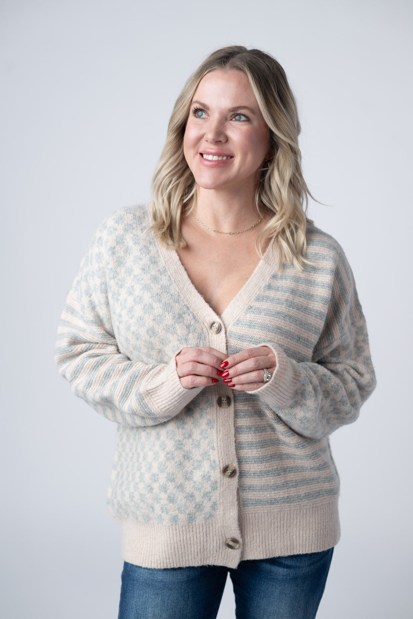 Woman wearing a Pattern Mix Neutral Cardigan with checkered and striped patterns in cream and dusty blue, button front and v-neckline, paired with jeans
