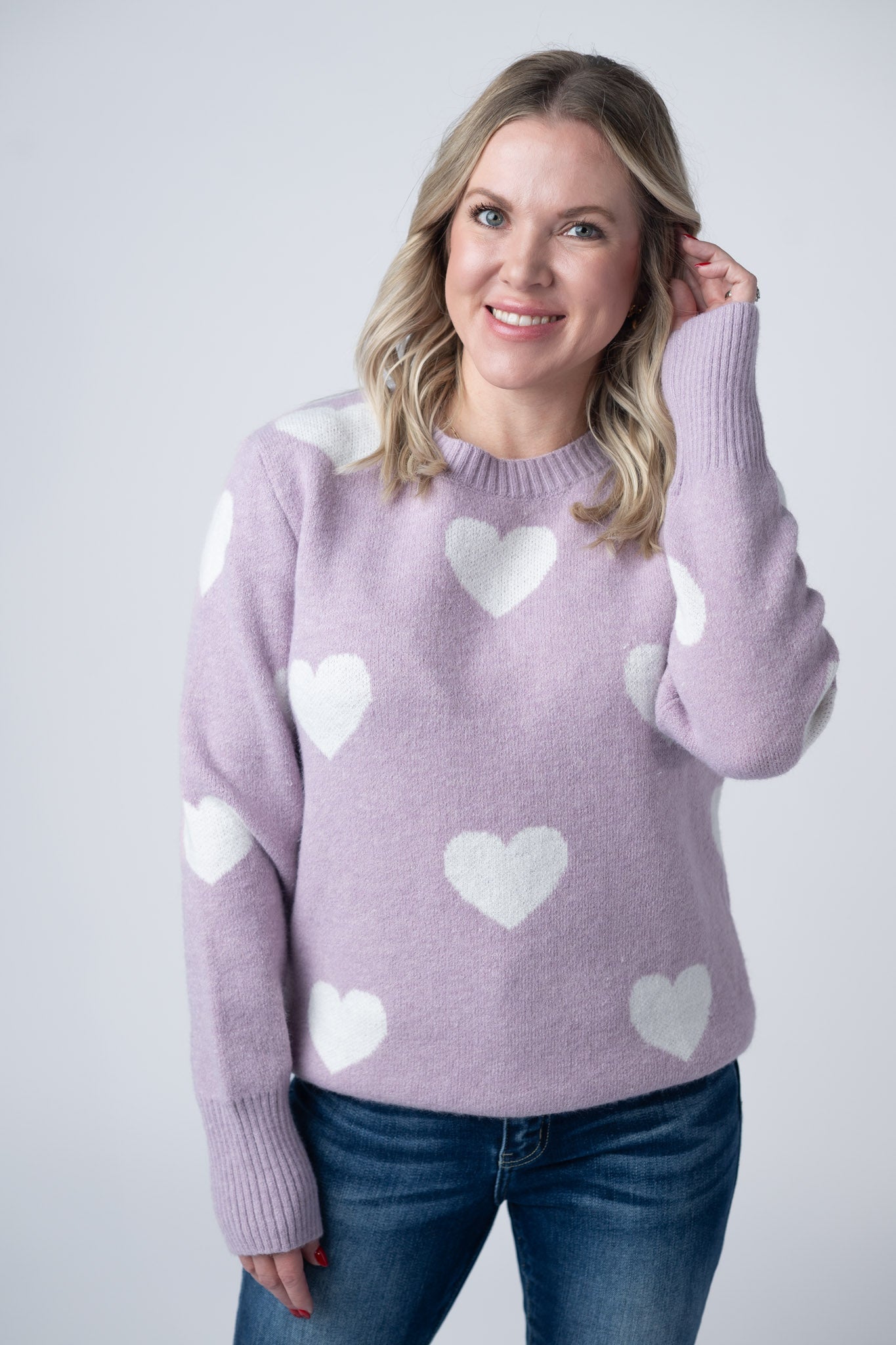 Woman wearing soft lavender sweater with white hearts pattern, crew neckline, and ribbed cuffs