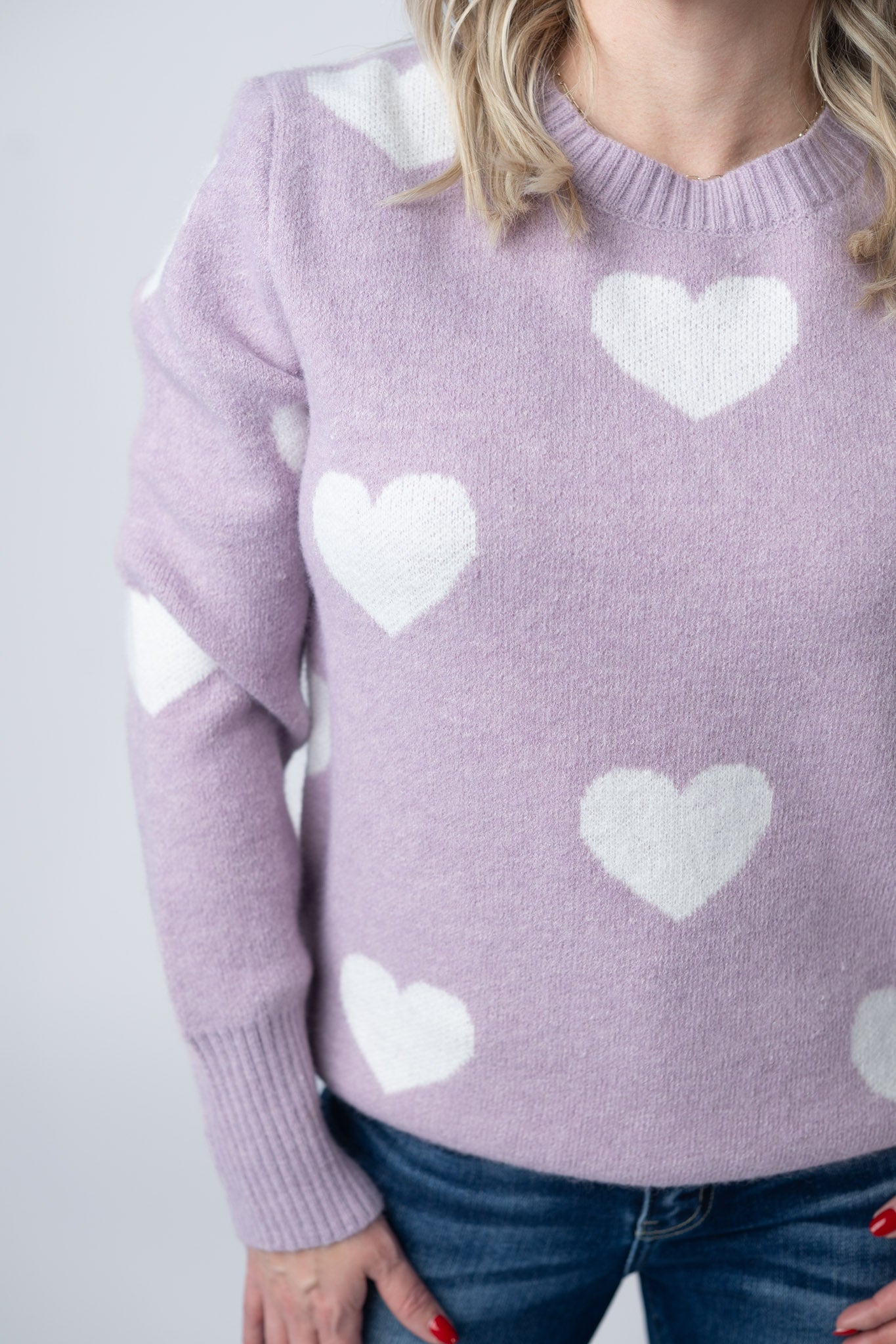 Woman wearing soft lavender sweater with white hearts pattern, crew neckline, and ribbed cuffs