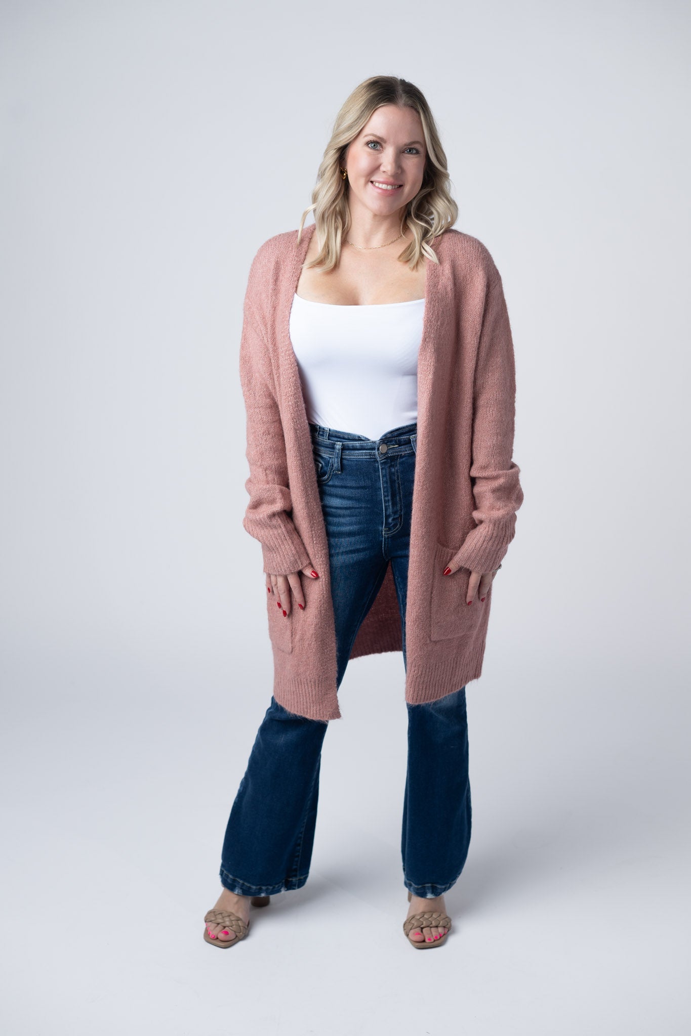 Woman wearing a dusty rose Madison Cozy Cardigan with front pockets, layered over a white tank and jeans