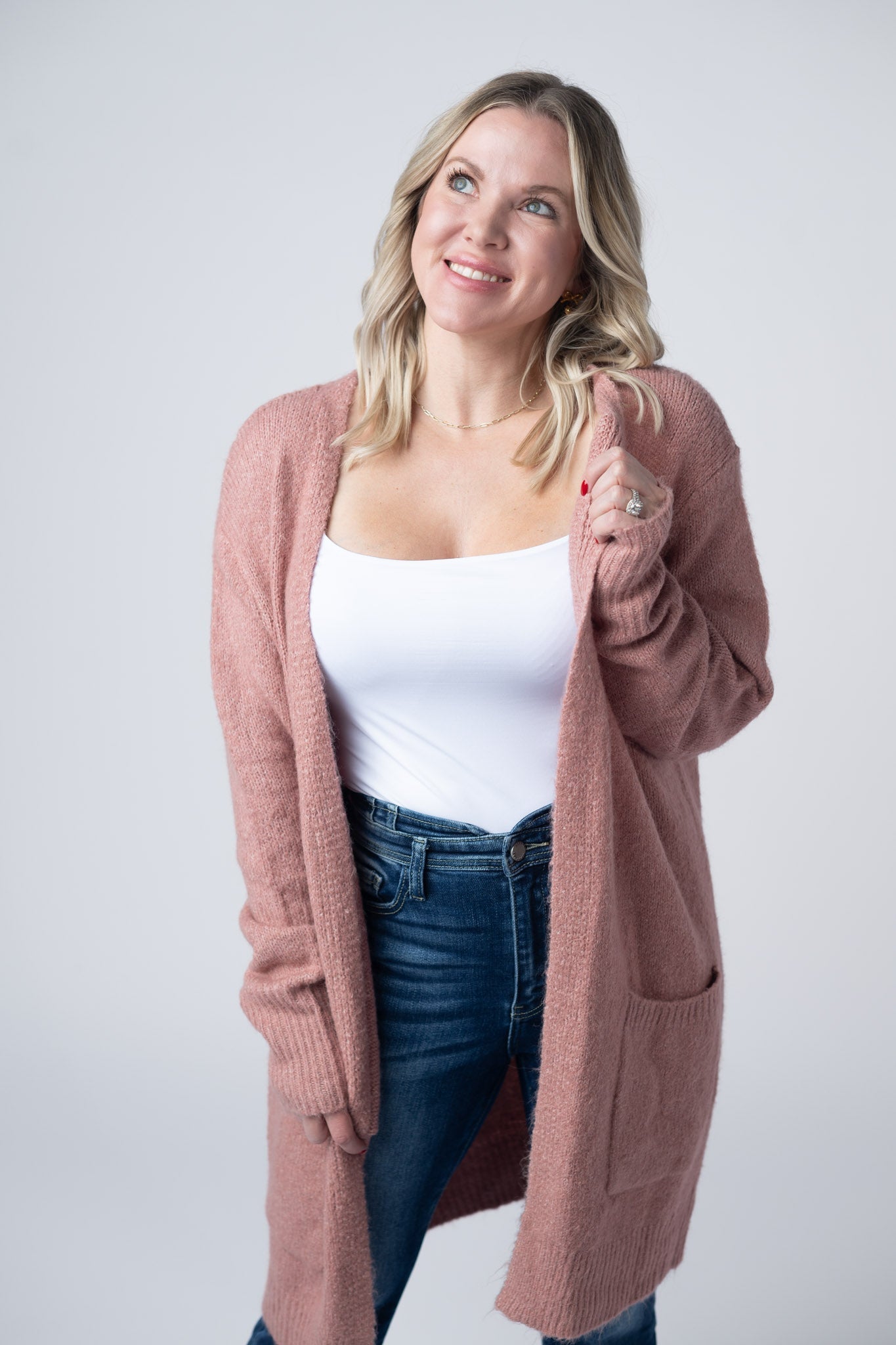 Woman wearing a dusty rose Madison Cozy Cardigan with front pockets, layered over a white tank and jeans