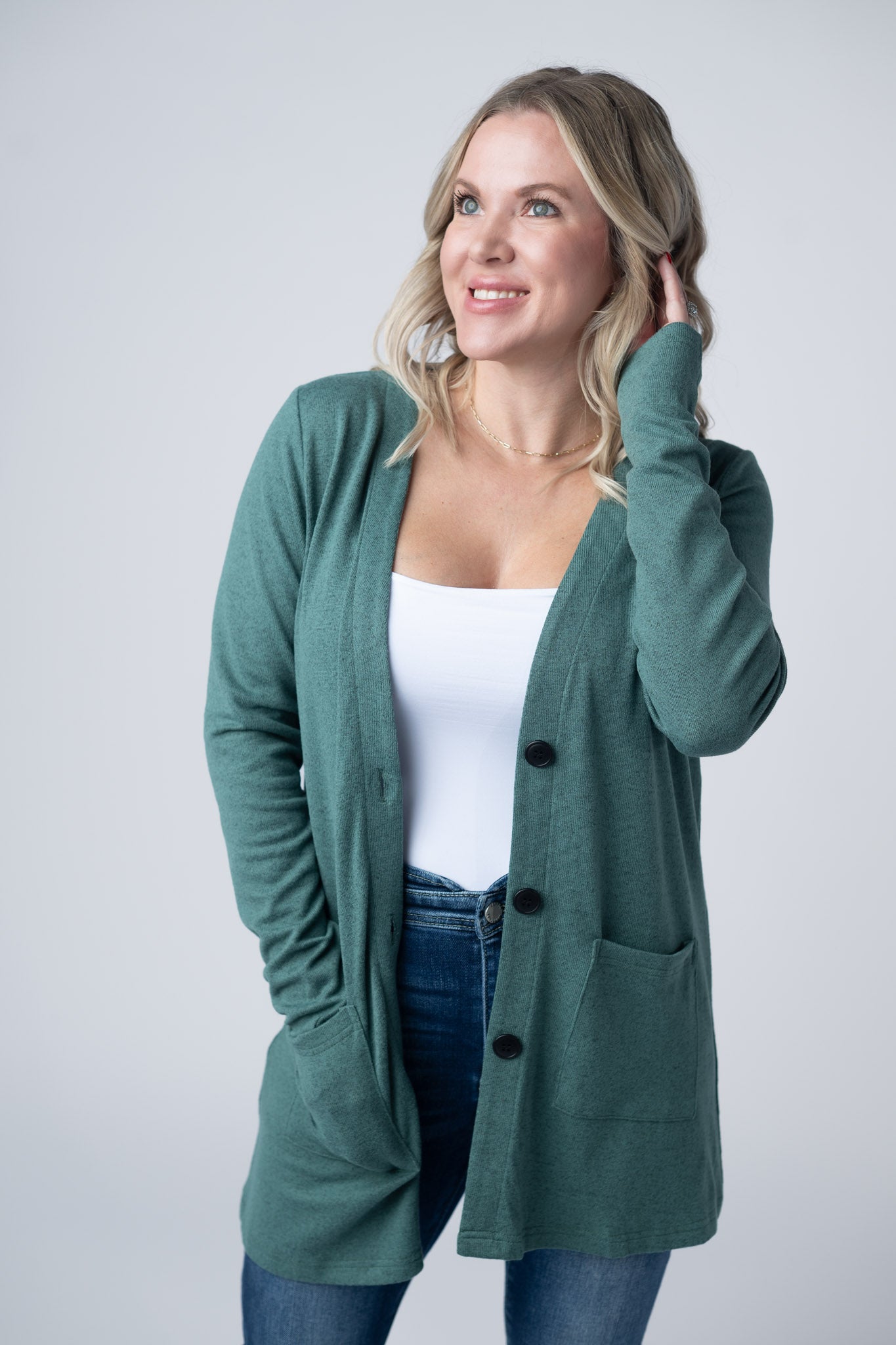 Woman wearing a sage green Cori Cardigan with button front and pockets, layered over a white tank and jeans