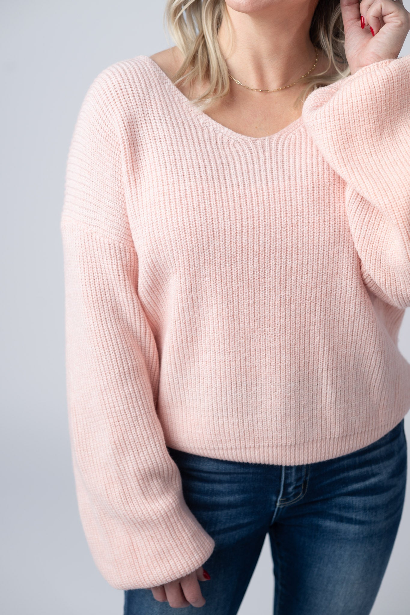 Woman wearing light pink ribbed knit sweater with v-neckline and satin bow tie detail on back