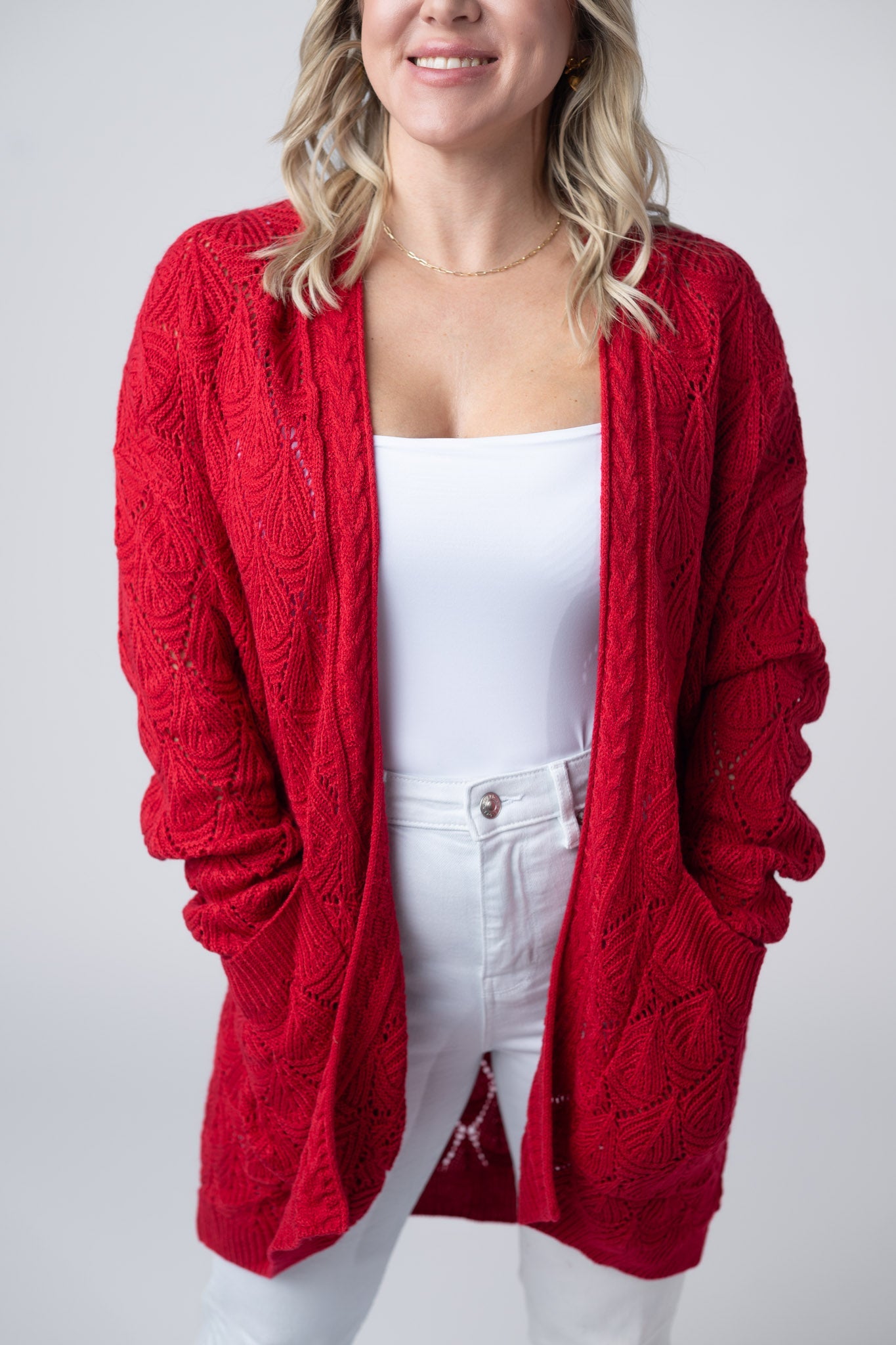 Woman wearing red open knit cardigan with open front, pockets, and relaxed fit over white top
