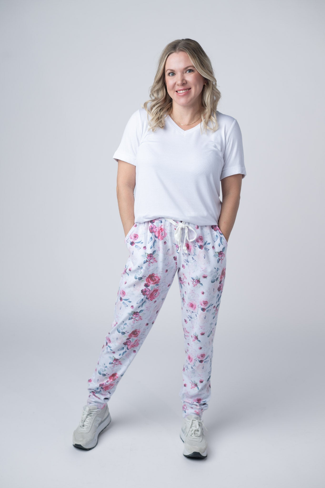 Woman wearing floral joggers with pink roses and blue leaves, white tee, and sneakers