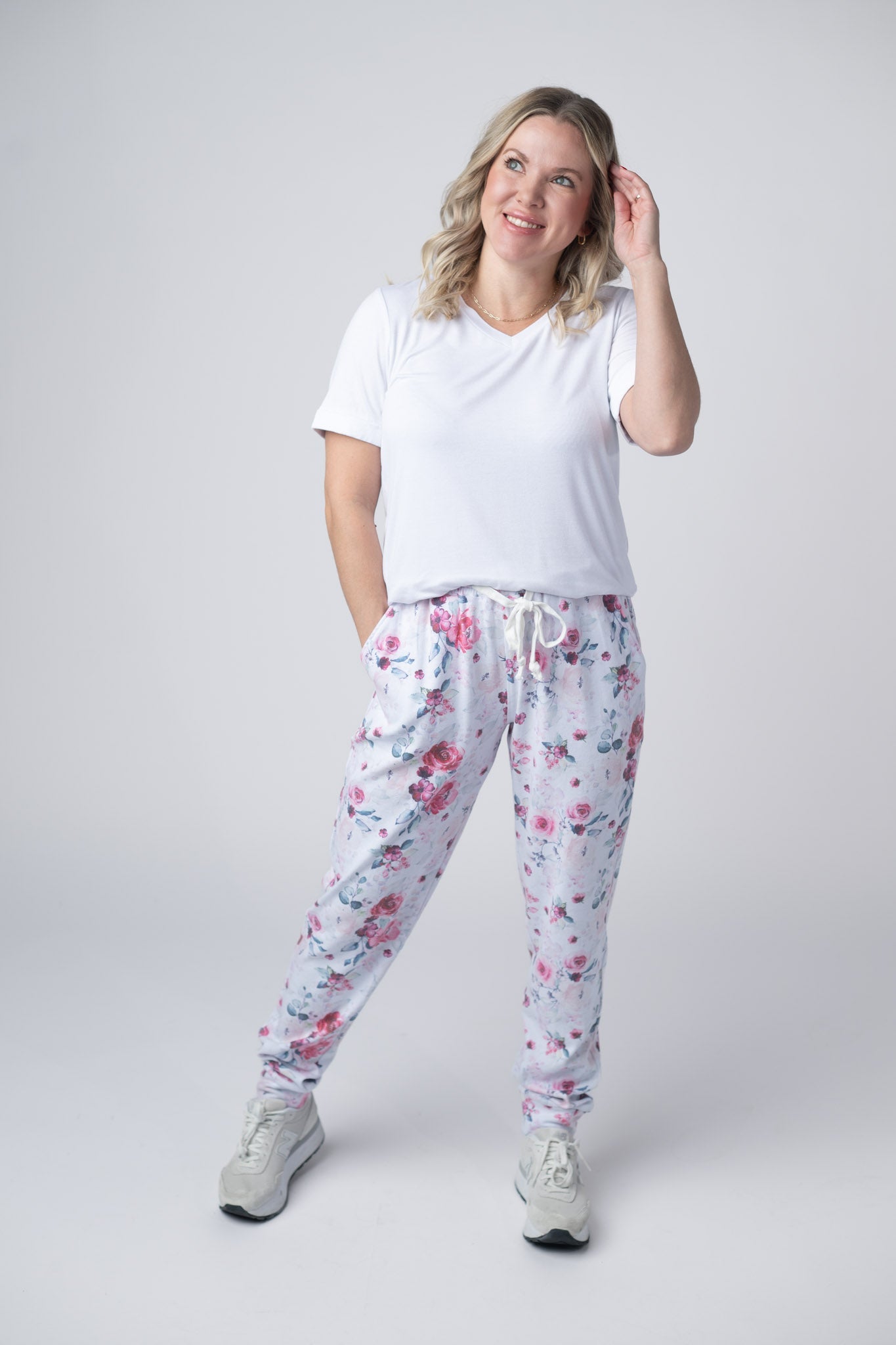 Woman wearing floral joggers with pink roses and blue leaves, white tee, and sneakers