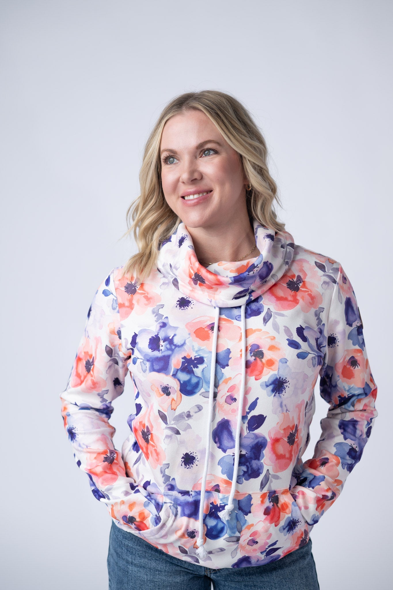 Woman wearing a white Soft Funnel Neck Sweatshirt with bold Sunset Watercolor Floral print in coral orange and navy blue, featuring a funnel neck with drawstrings and kangaroo pocket