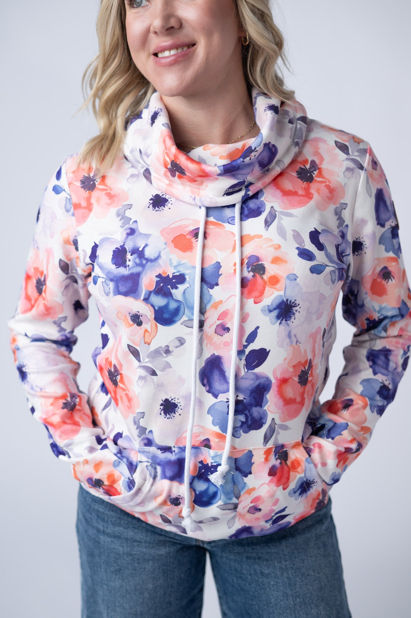 Woman wearing a white Soft Funnel Neck Sweatshirt with bold Sunset Watercolor Floral print in coral orange and navy blue, featuring a funnel neck with drawstrings and kangaroo pocket