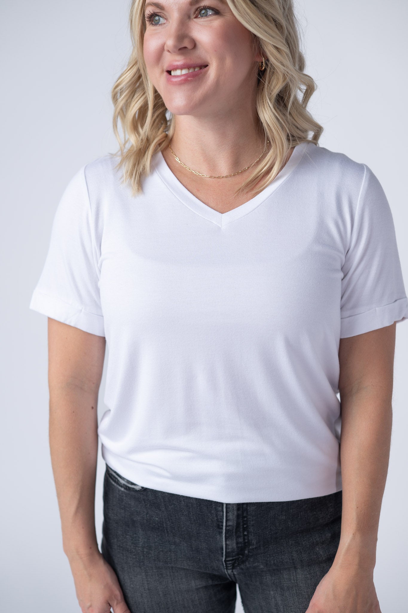 Women's white v-neck tee with short cuffed sleeves and relaxed fit styled with gray jeans