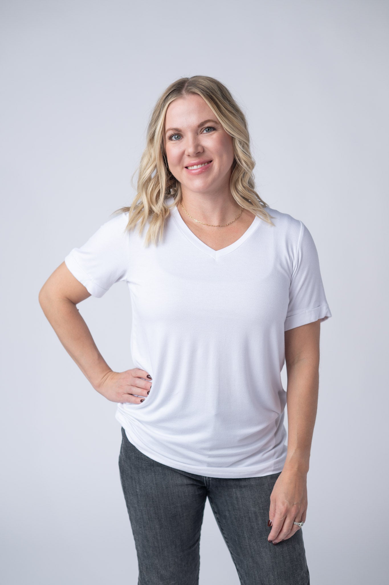 Women's white v-neck tee with short cuffed sleeves and relaxed fit styled with gray jeans