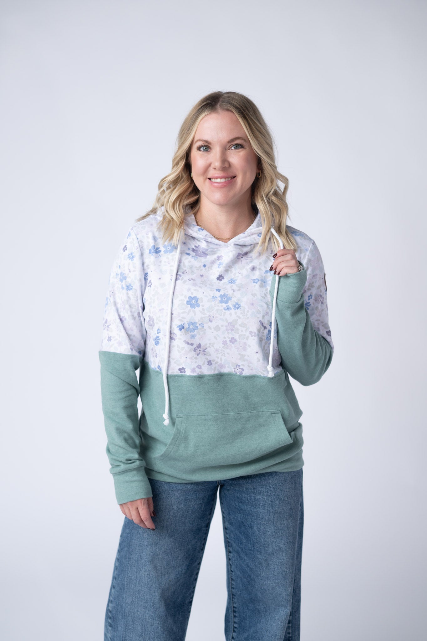 Woman wearing colorblock pullover hoodie with soft blue and lavender floral print on top and sage green bottom with kangaroo pocket