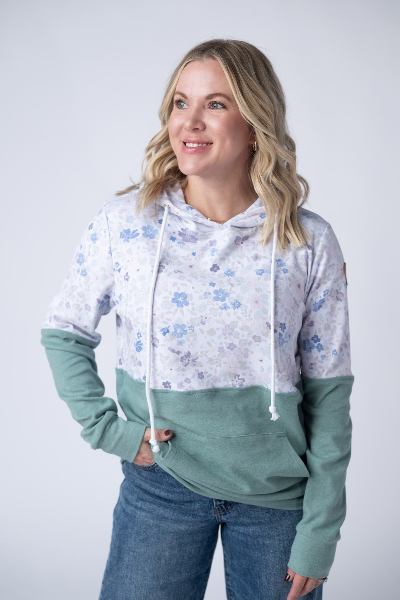 Woman wearing colorblock pullover hoodie with soft blue and lavender floral print on top and sage green bottom with kangaroo pocket