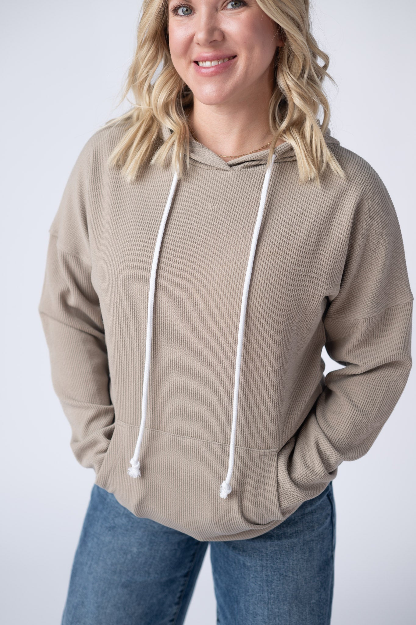 Woman wearing a mocha brown Kacey Ribbed Hoodie with white drawstrings, kangaroo pocket, and ribbed texture, paired with jeans